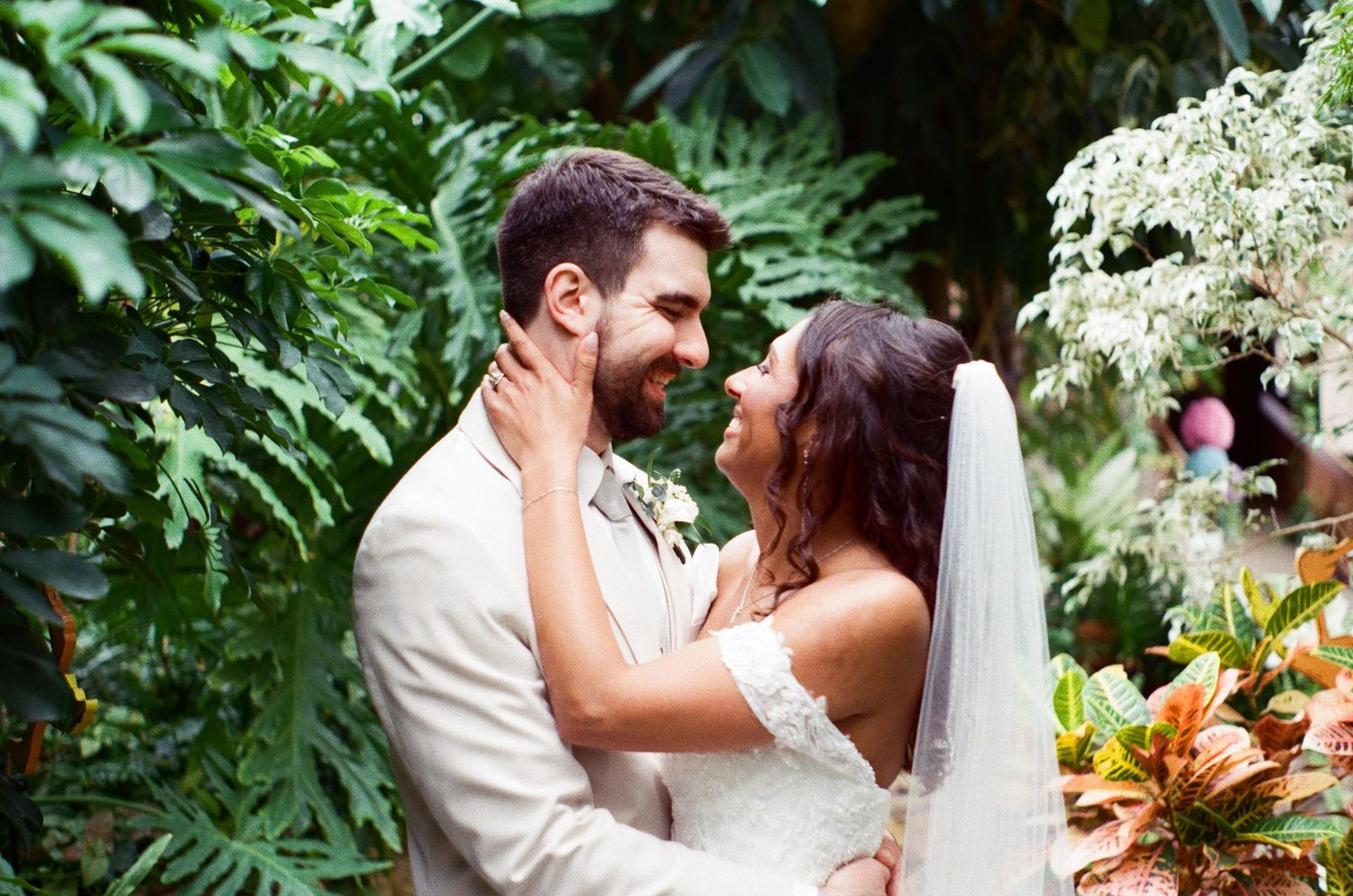 Bride and groom share a romantic moment surrounded by lush tropical greenery at their outdoor wedding ceremony.