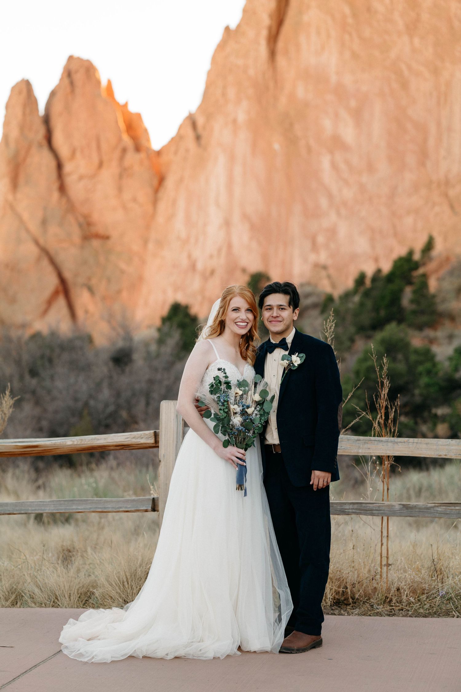 Wedding couple poses against stunning red rock formations at sunset.