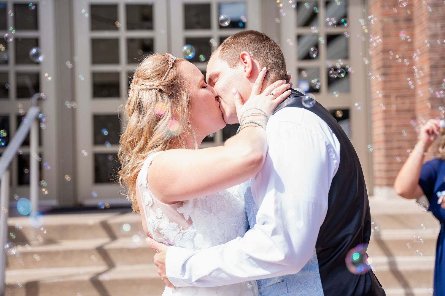 Couple in wedding attire sharing romantic moments outside a brick building.
