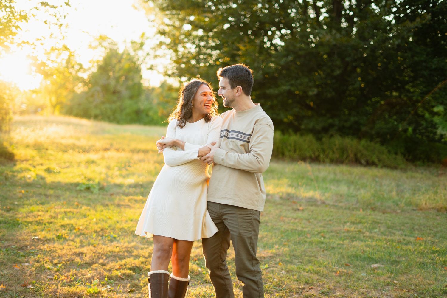 A romantic sunset maternity photo session in a grassy field with warm golden lighting.