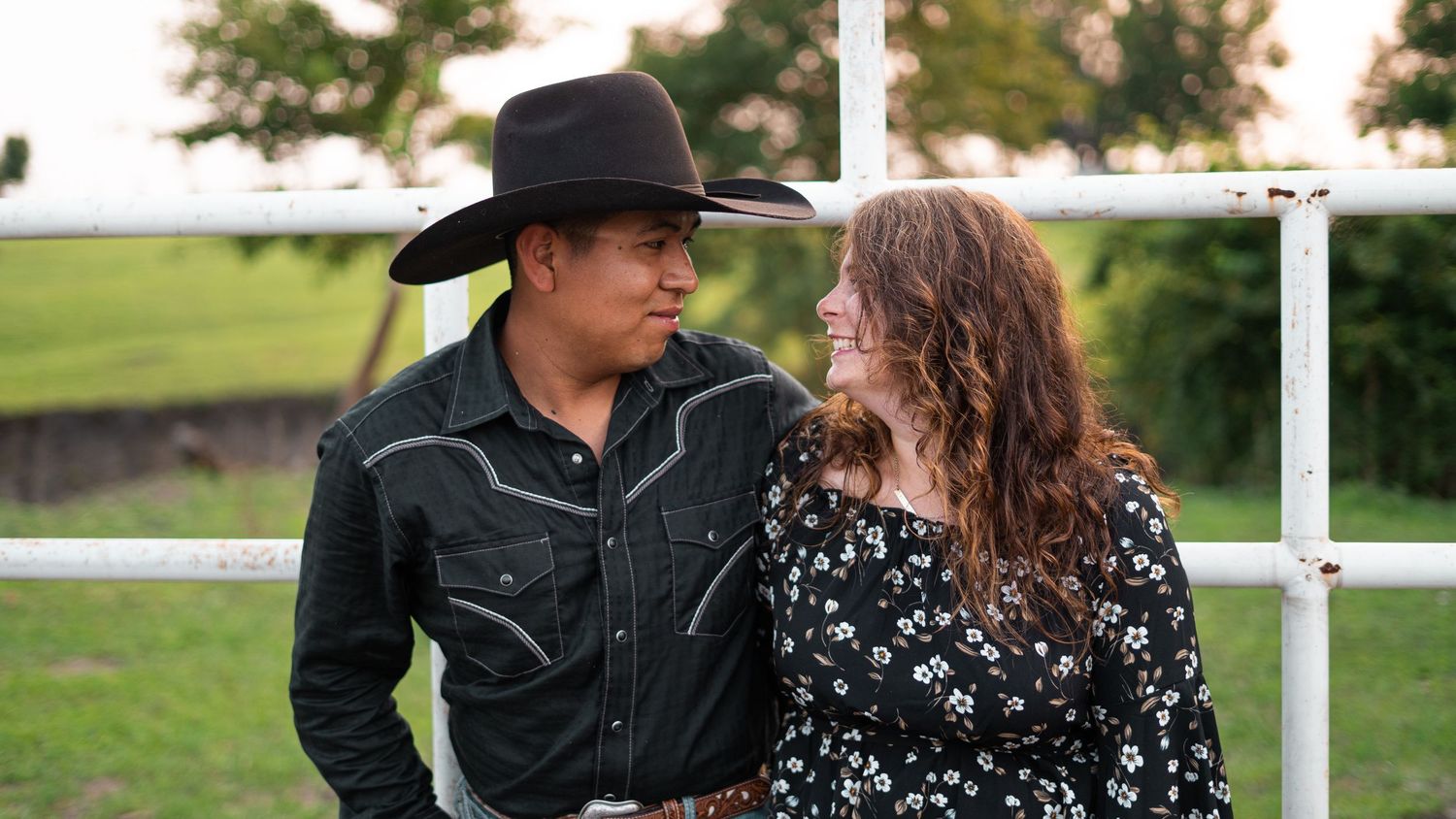 A couple in western attire shares romantic moments in a field at sunset.