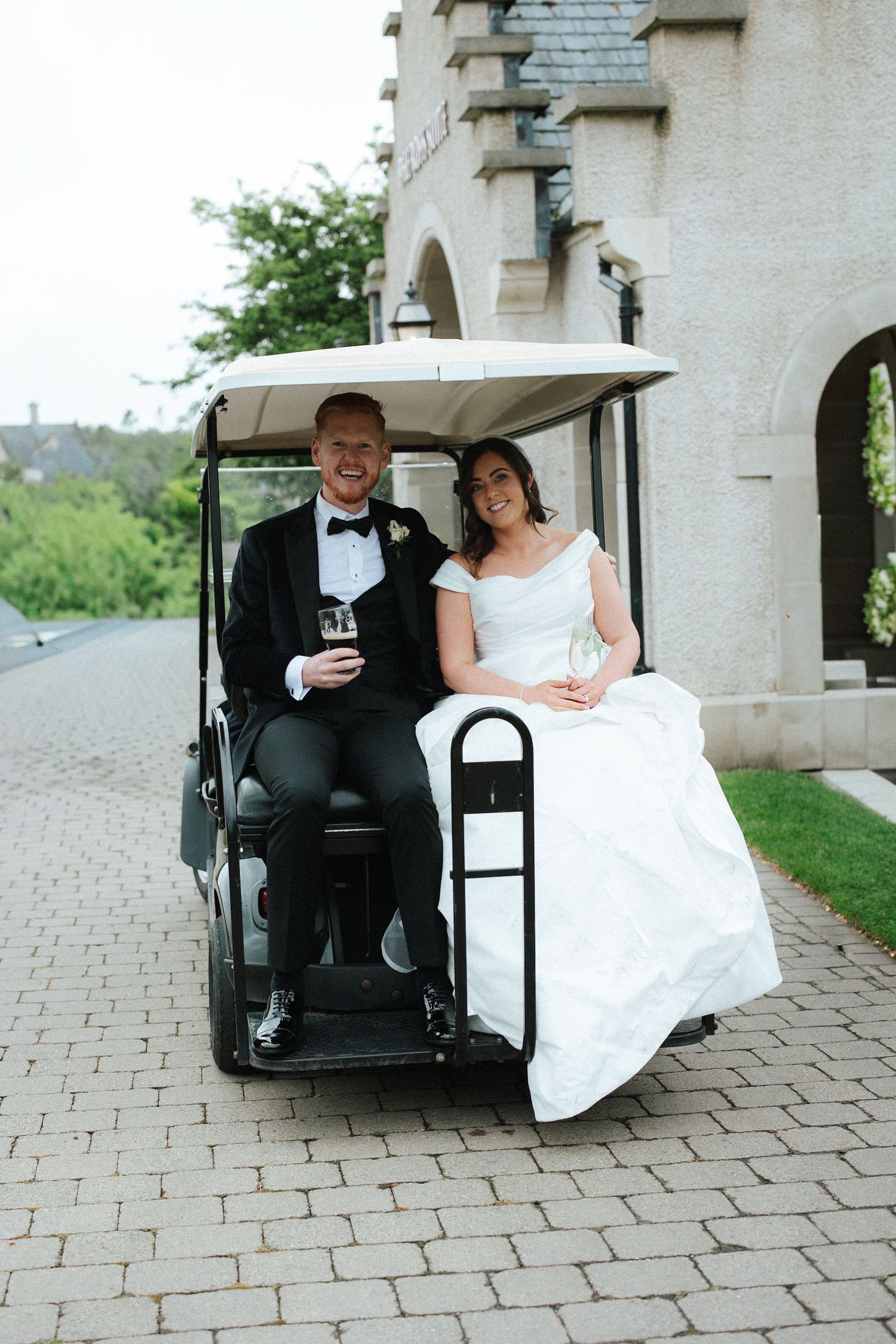Bride and groom smiling on a golf cart outside a castle venue on their wedding day.