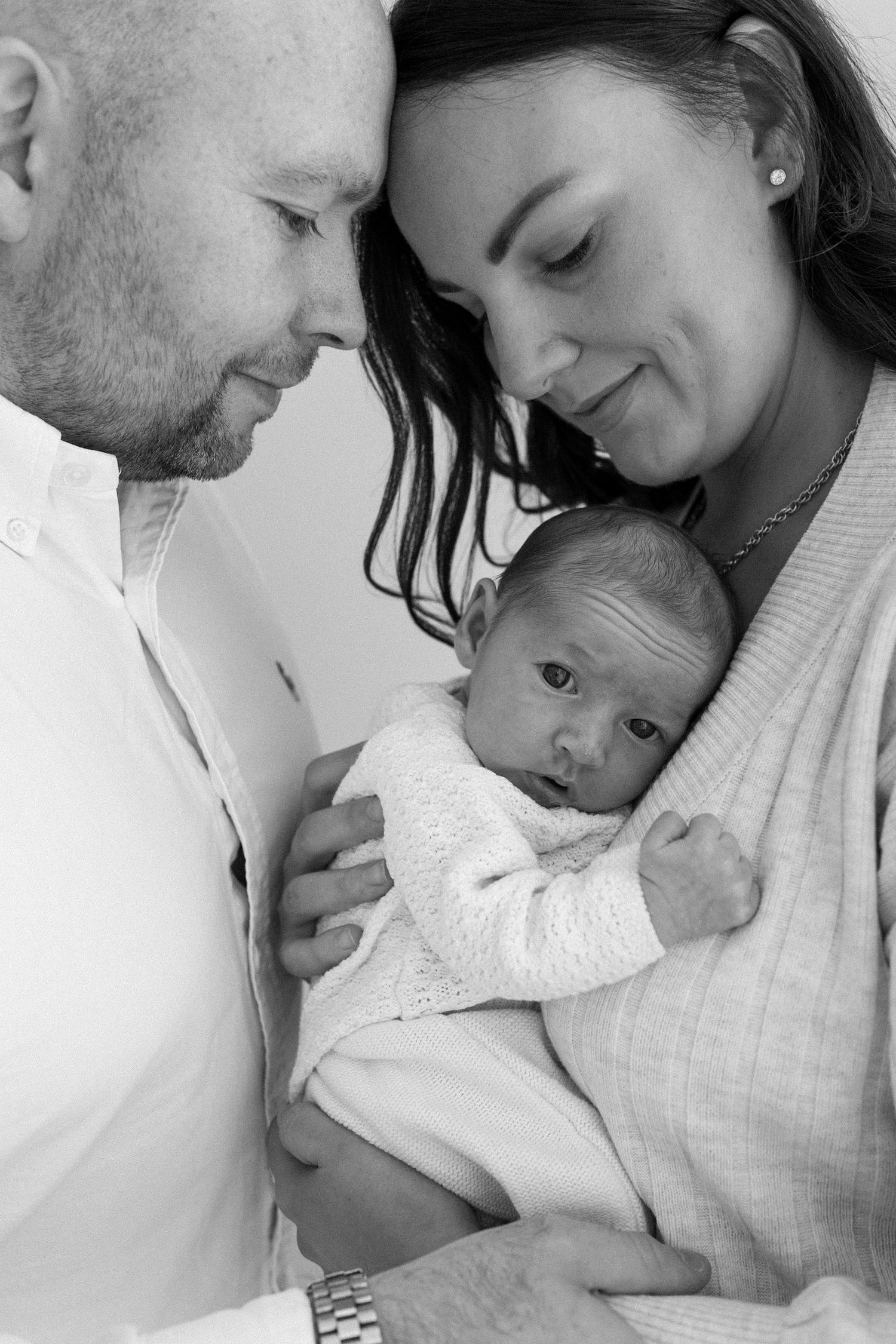 Black and white portrait of smiling parents holding their alert newborn baby.