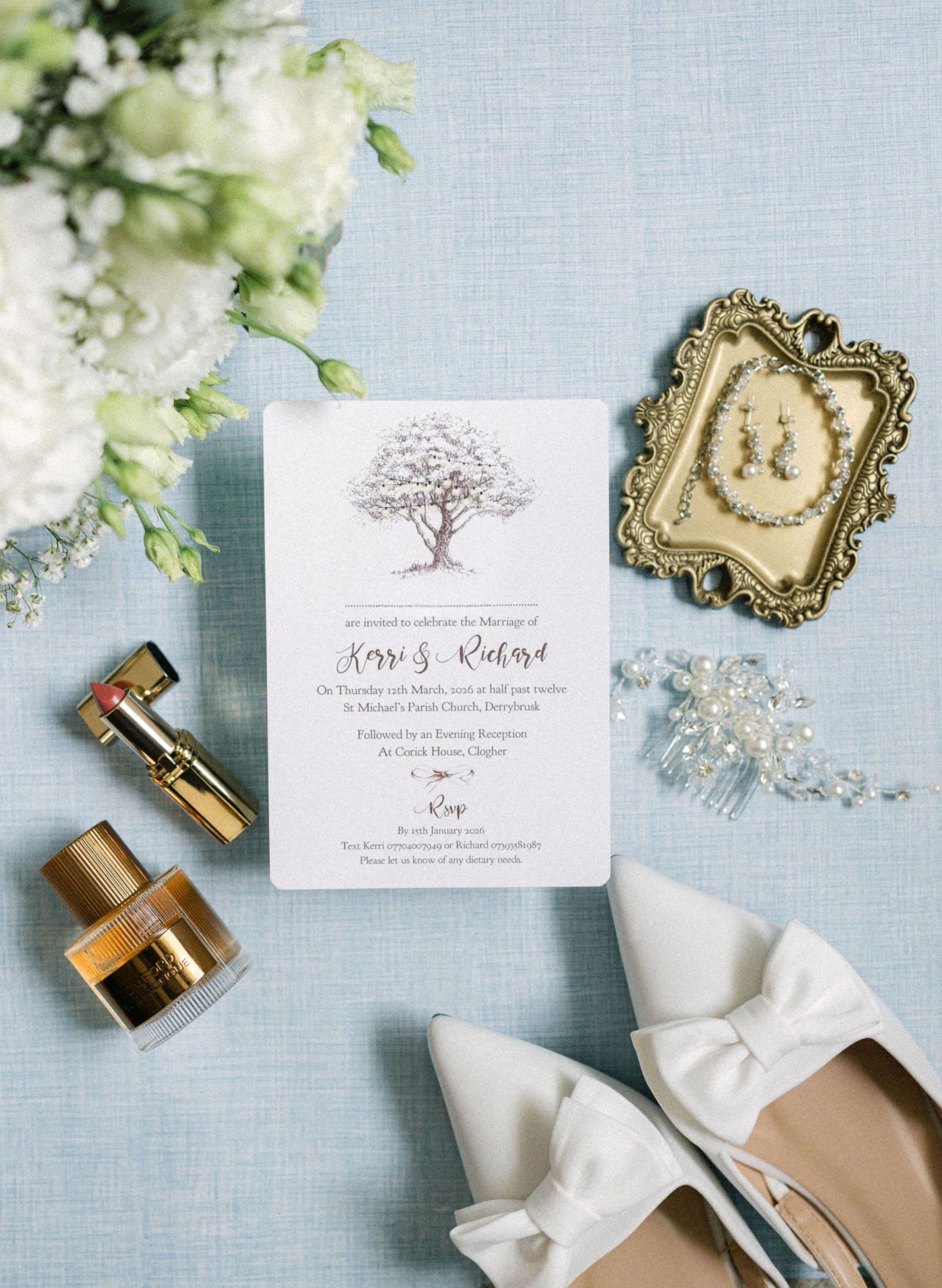 Elegant wedding flat lay featuring floral invitation, white bow heels, gold jewelry, and white flower bouquet.