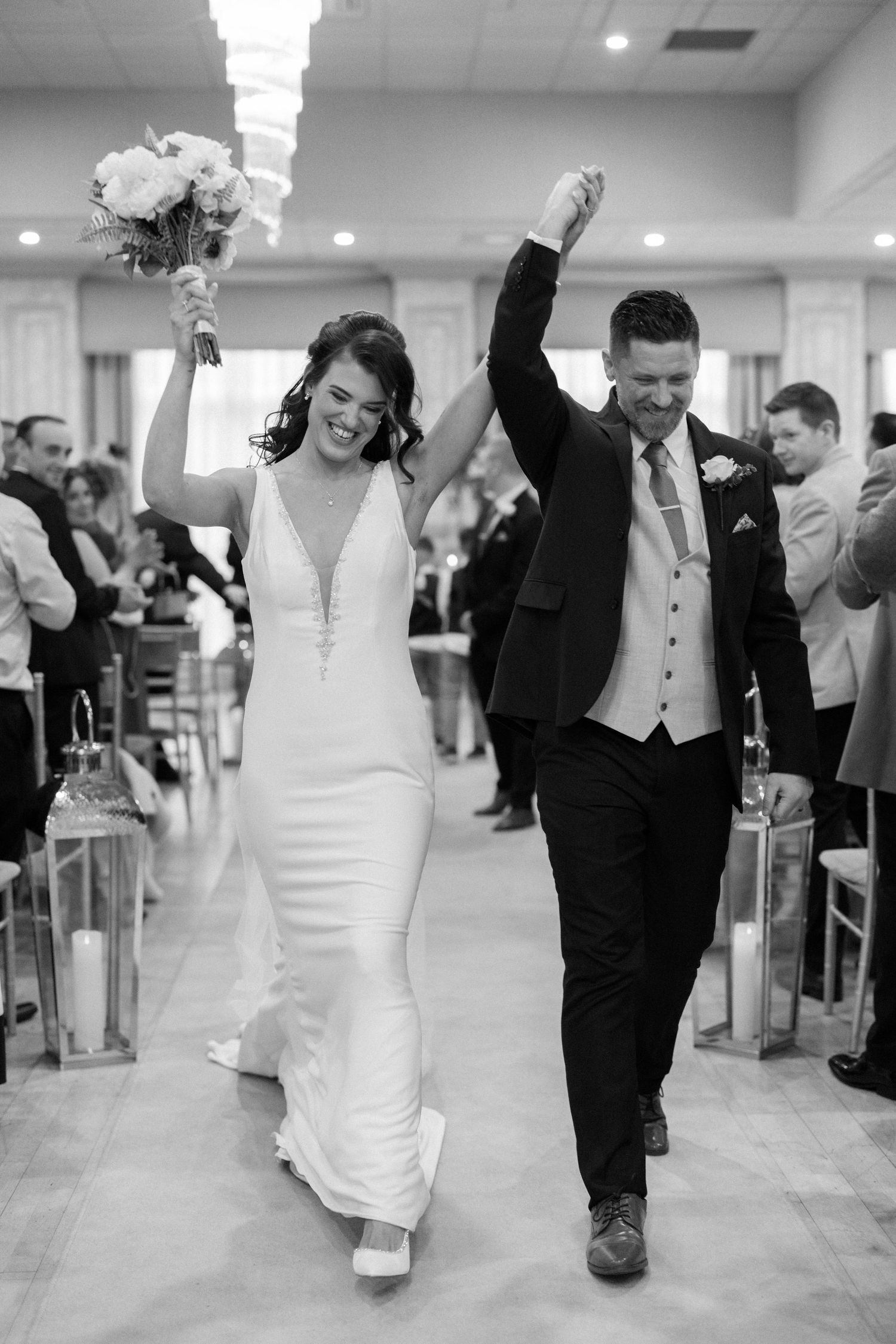 Joyful newlyweds celebrate their wedding ceremony exit, raising hands triumphantly as guests cheer in elegant venue.