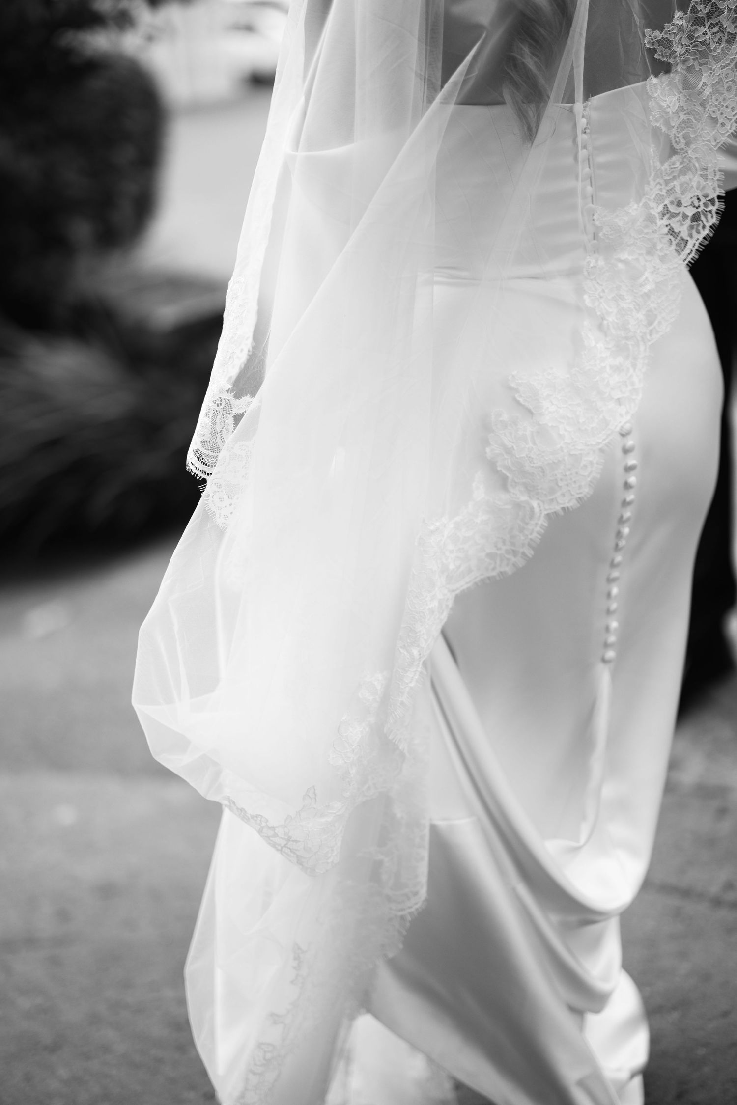 Black and white photo of a bride in a white wedding gown with lace-trimmed veil and pearl button details.