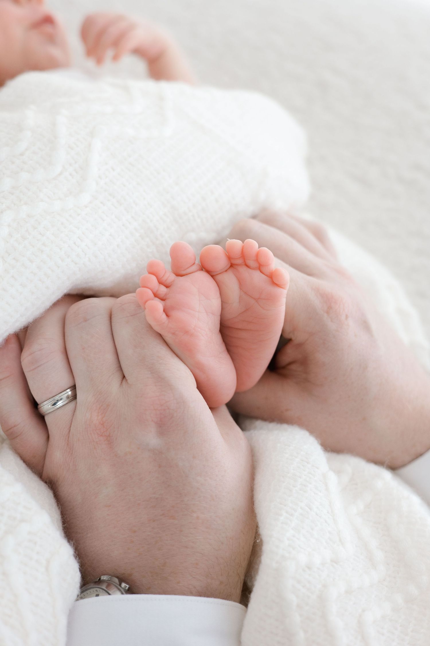 Close-up of adult hands gently holding tiny newborn baby feet wrapped in a soft white knit blanket.