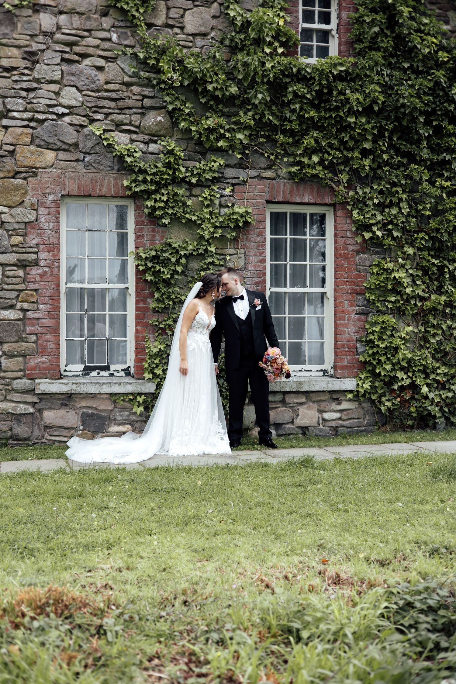 Bride and groom sharing a romantic moment in front of an ivy-covered stone building at their wedding.