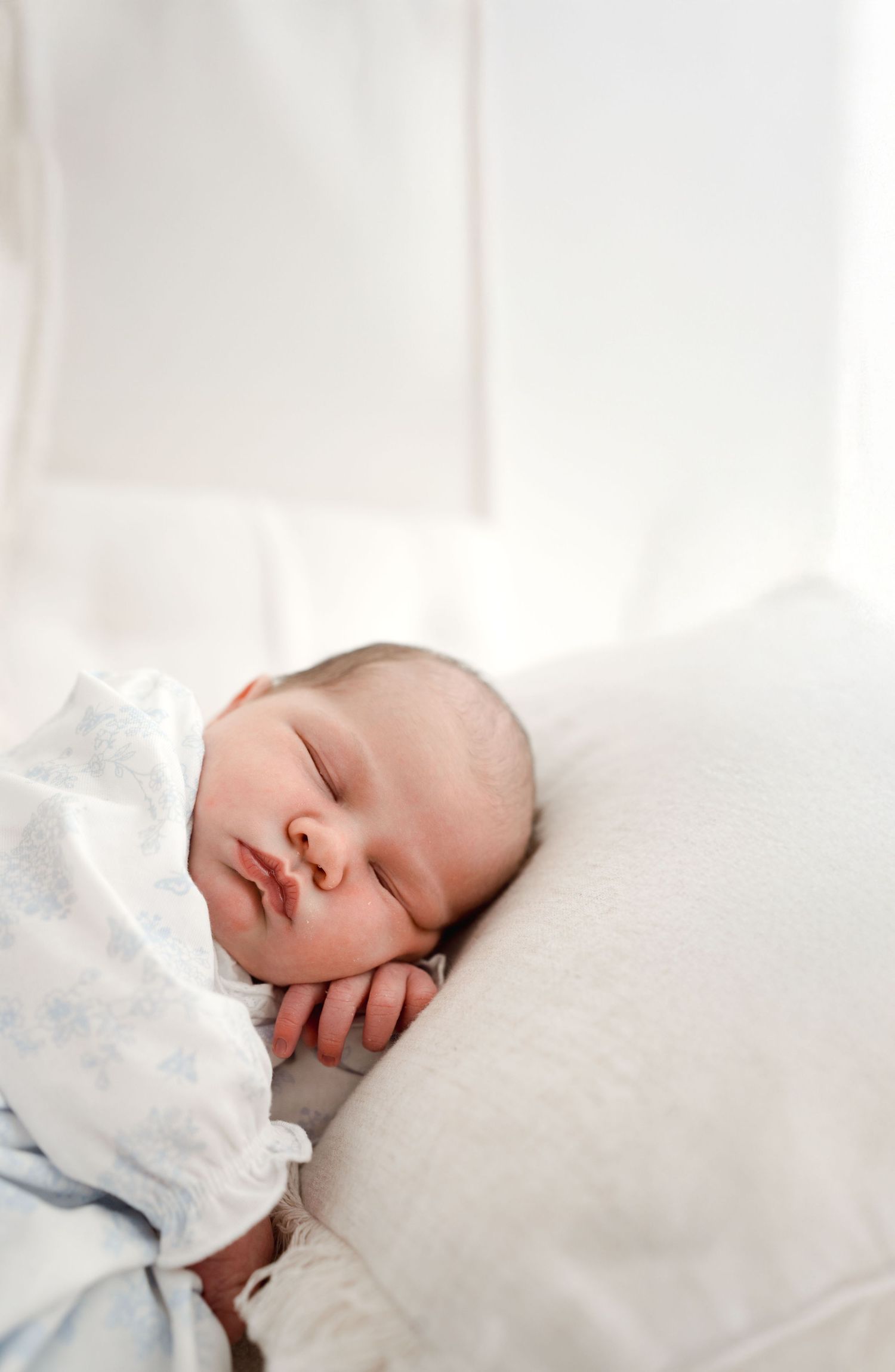 Peaceful newborn baby sleeping on white pillow wrapped in soft light blue blanket.