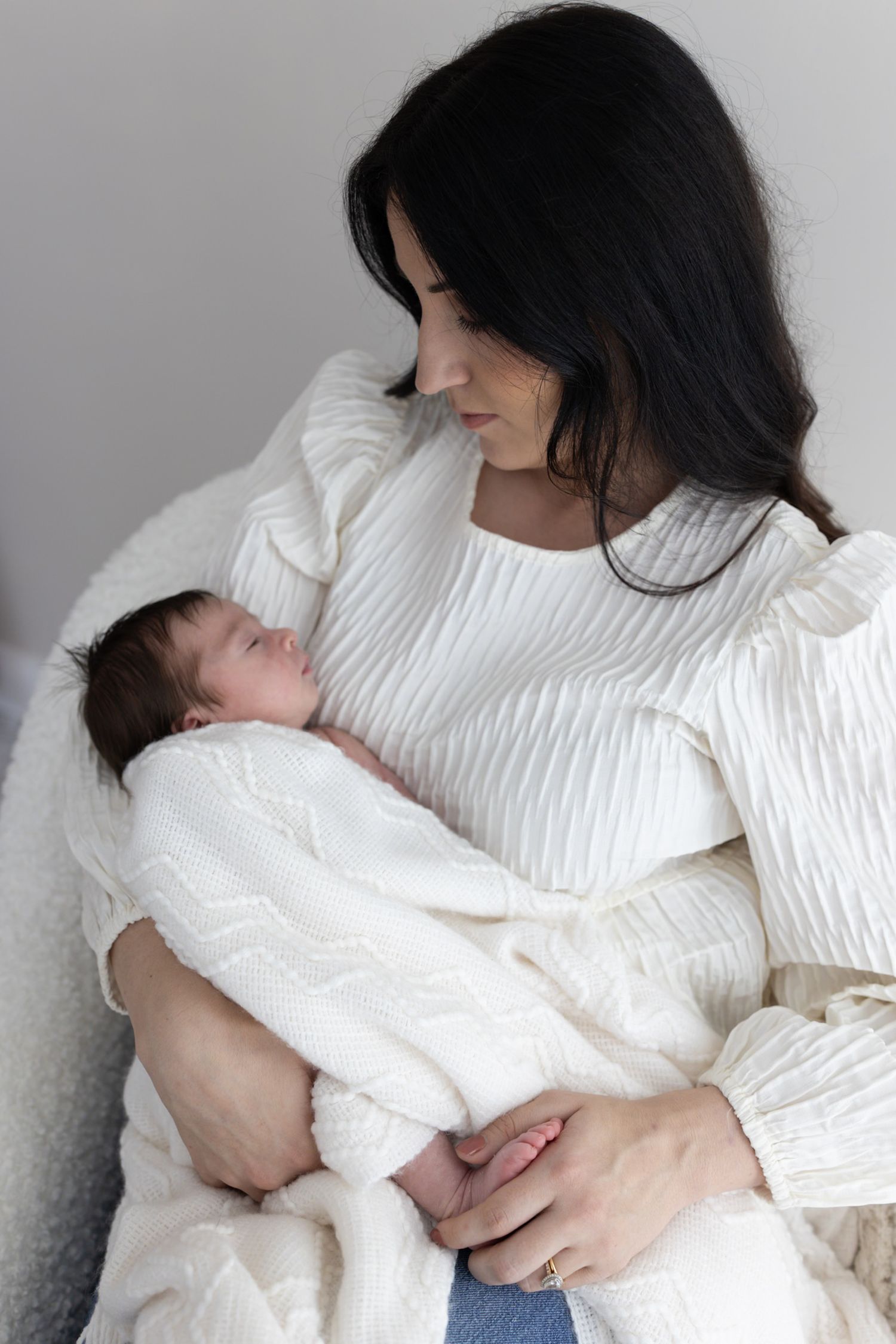 Mother with dark hair in white top gently cradling her peaceful swaddled newborn baby.