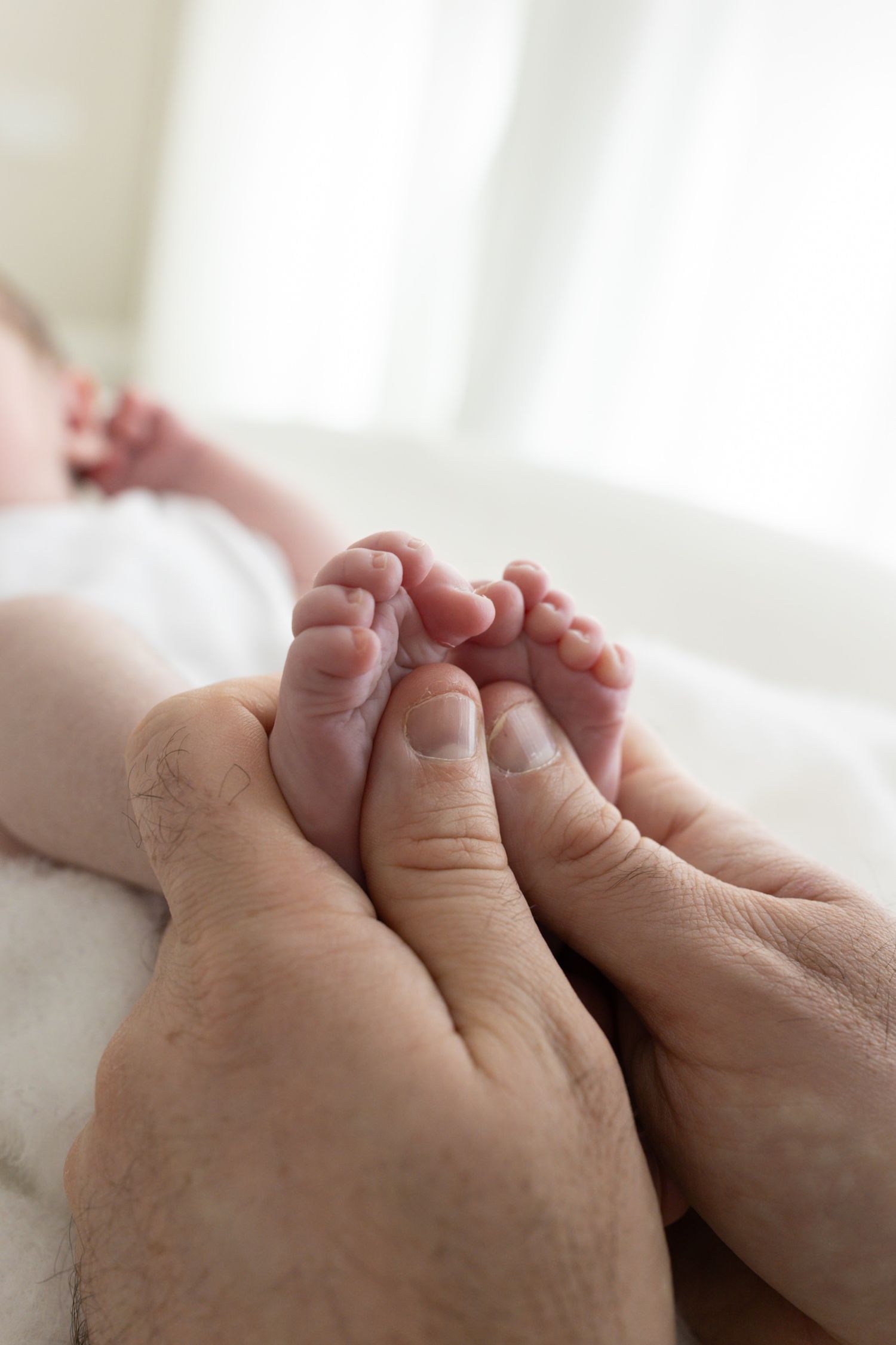 Close-up of fathers hands gently holding tiny newborn baby feet.