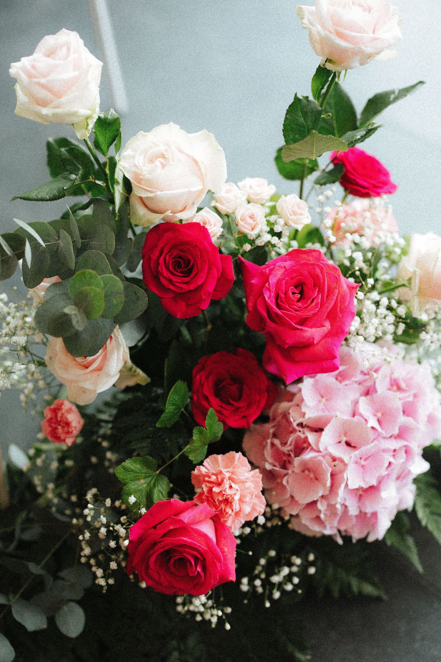 Elegant bouquet featuring red and pink roses, hydrangeas, carnations, and baby's breath with lush green foliage.