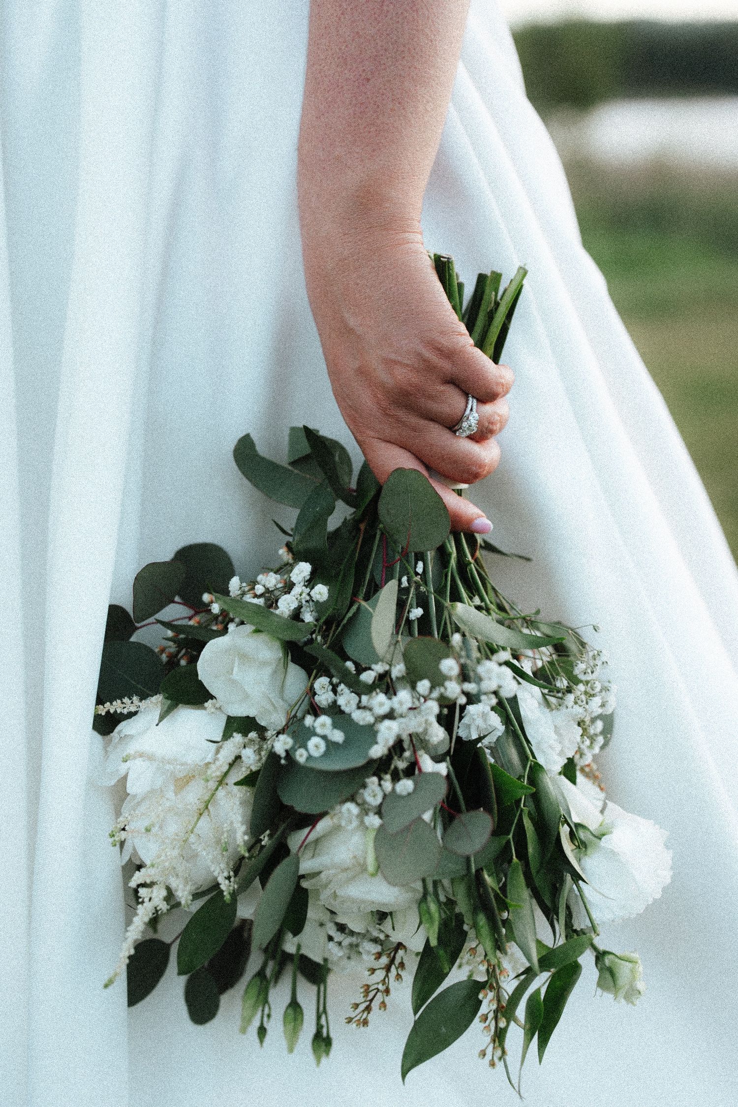 Bride holding a white wedding bouquet with roses, eucalyptus, and baby's breath while wearing a white gown.