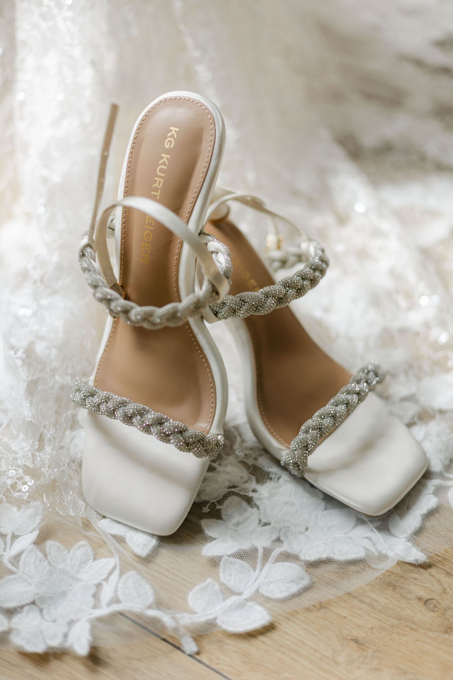Elegant white bridal heels with braided crystal straps by KG Kurt Geiger on lace wedding dress.