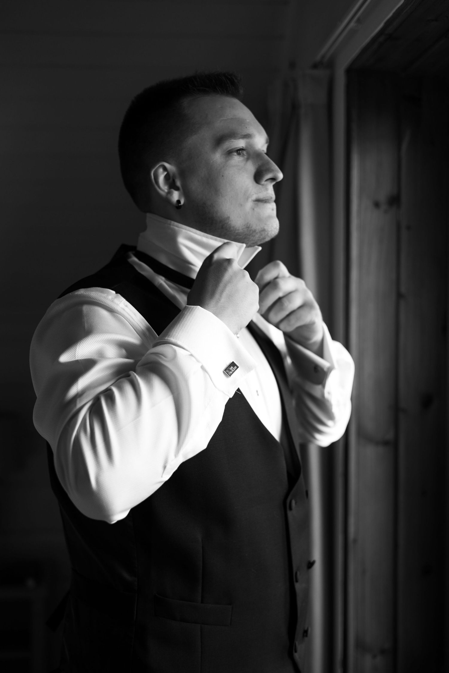 Black and white portrait of a groom adjusting his tie while getting ready for his wedding.