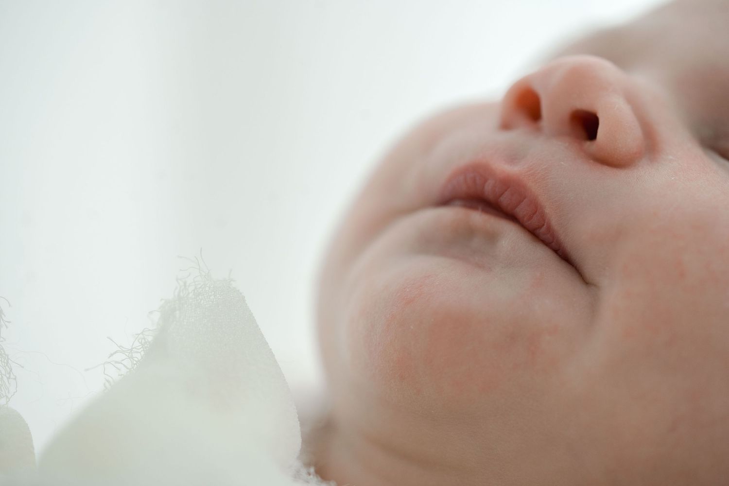 Extreme close-up of a sleeping newborns delicate facial features against soft white background.