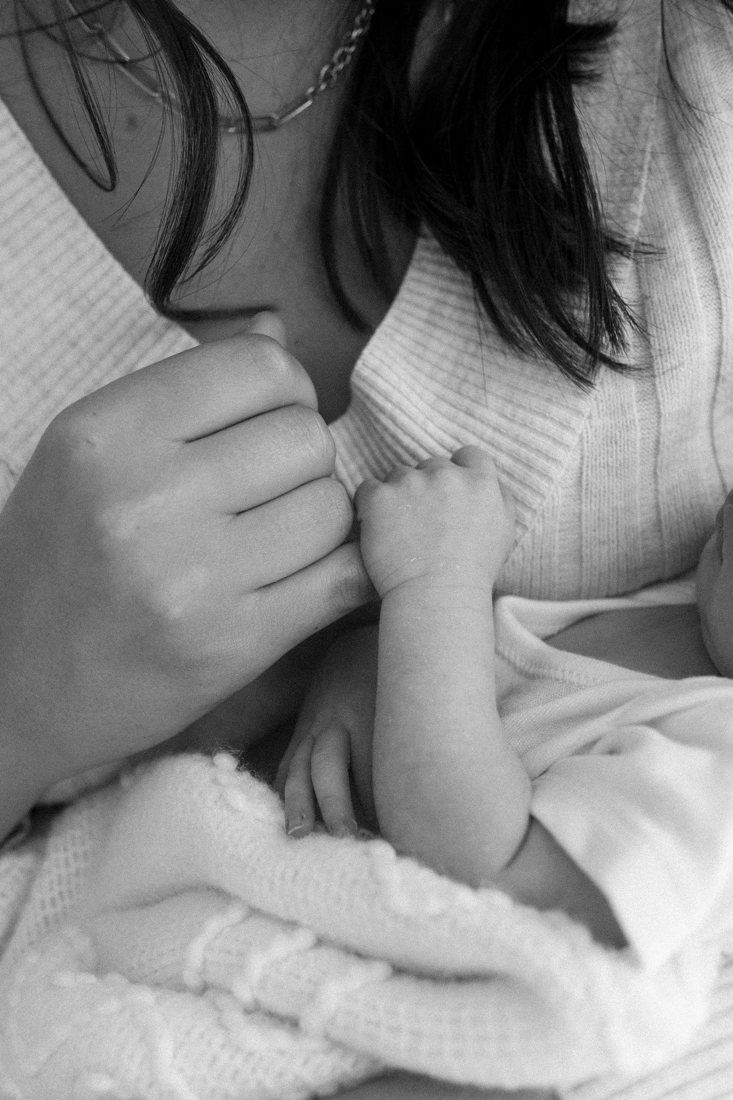 Black and white close-up of a newborn baby grasping mothers finger gently.