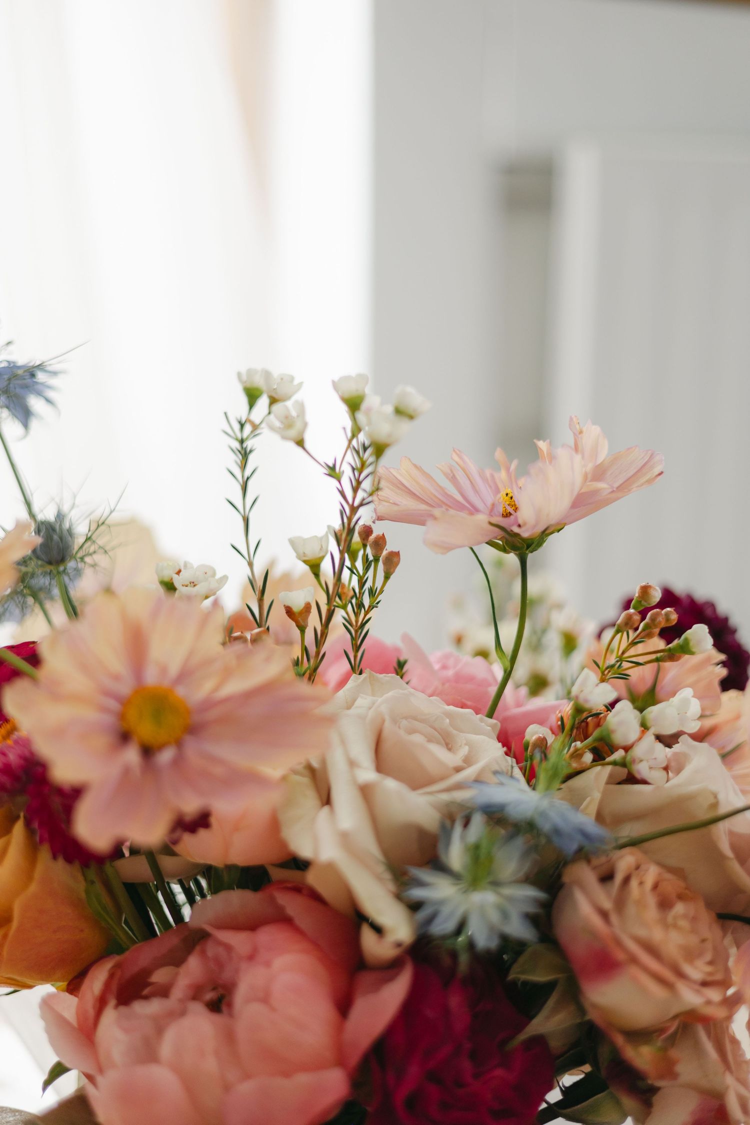 Close-up of a lush bridal bouquet featuring peonies, roses, cosmos, and blue thistle flowers.