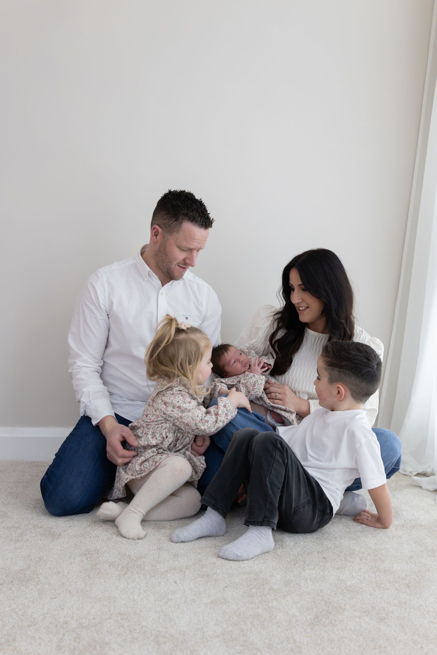 Family of five sitting on floor, parents with three children admiring their newborn baby.
