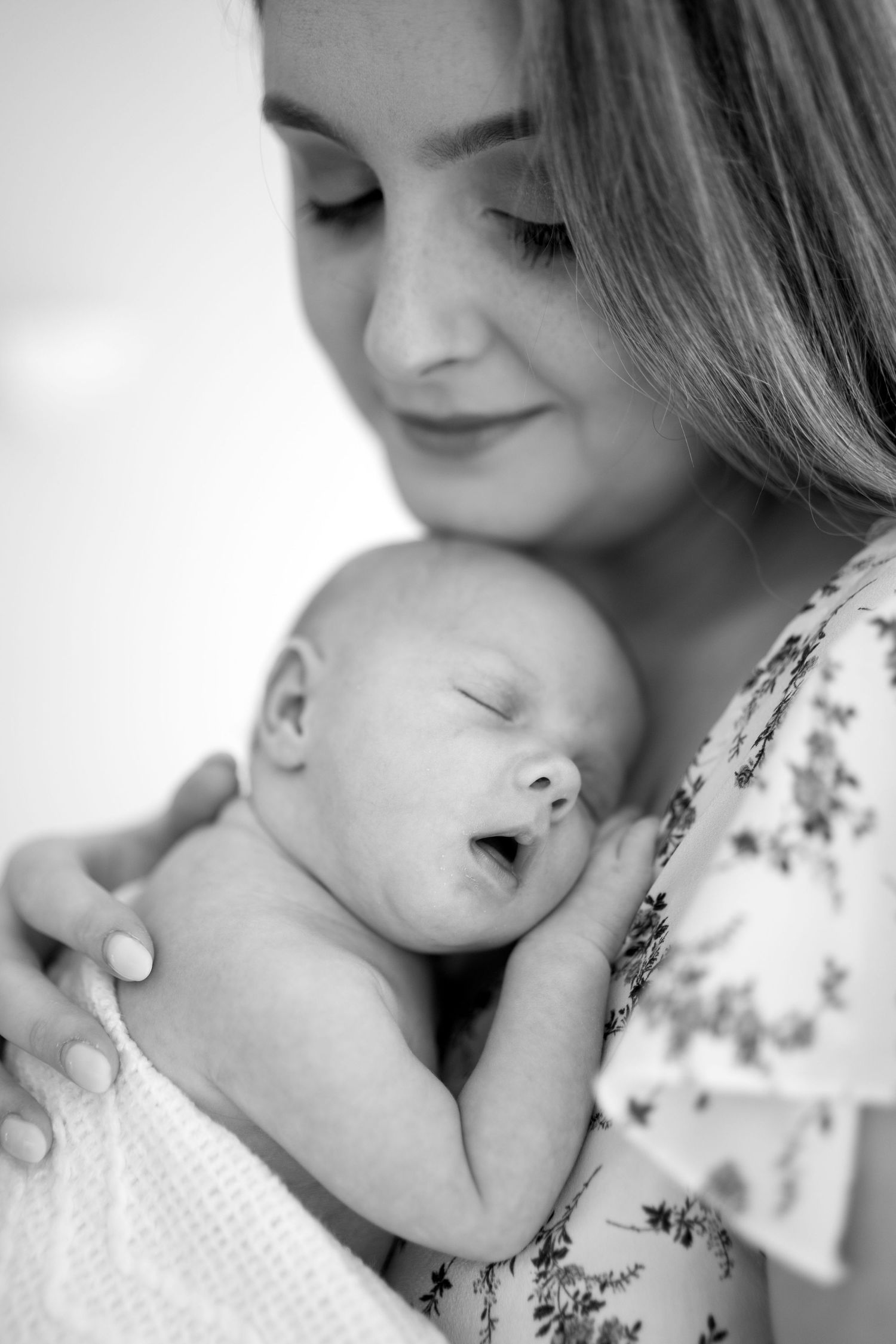 Black and white portrait of a mother lovingly holding her yawning newborn baby close to her chest.
