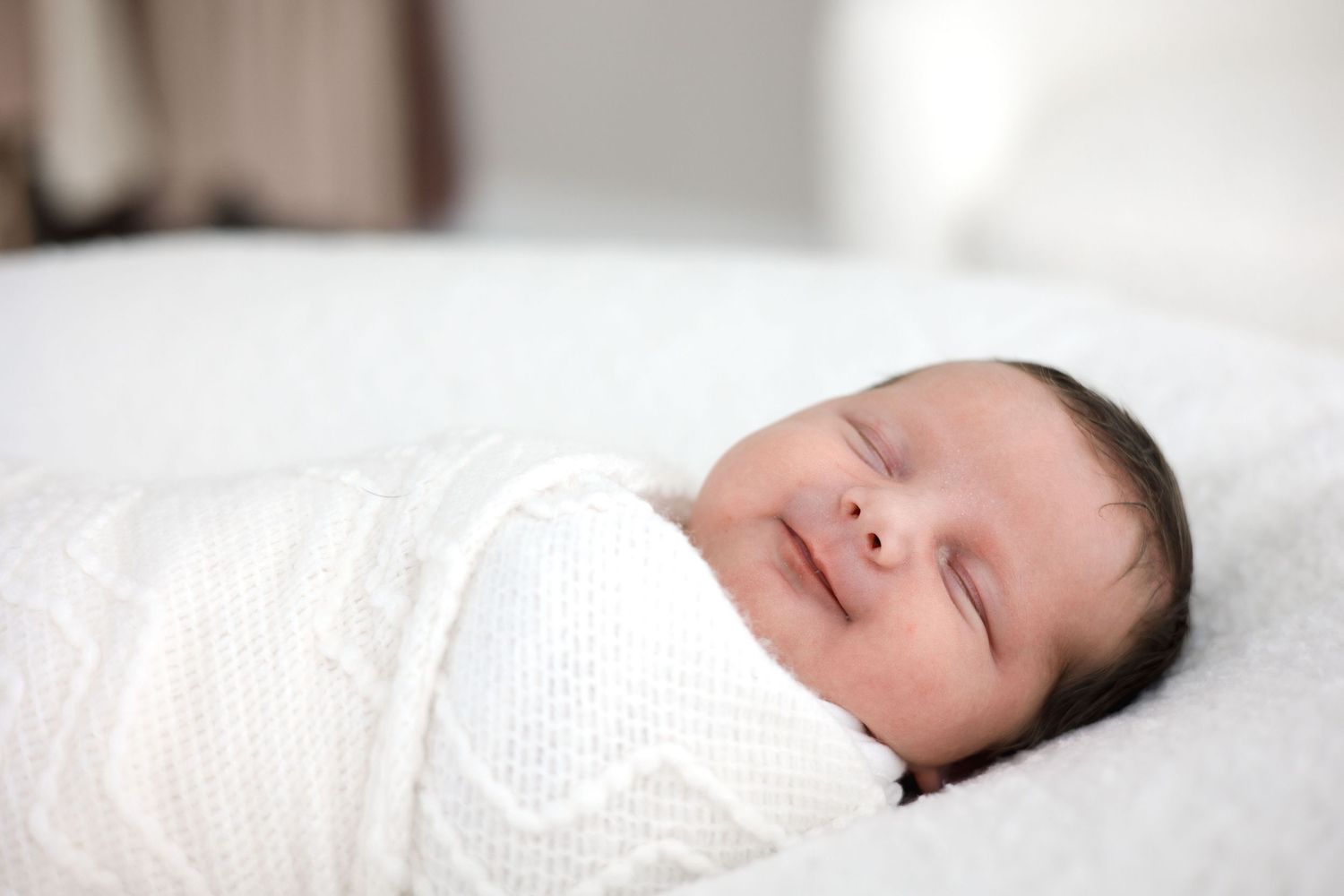 Peaceful newborn baby swaddled in white blanket sleeping with a gentle smile.