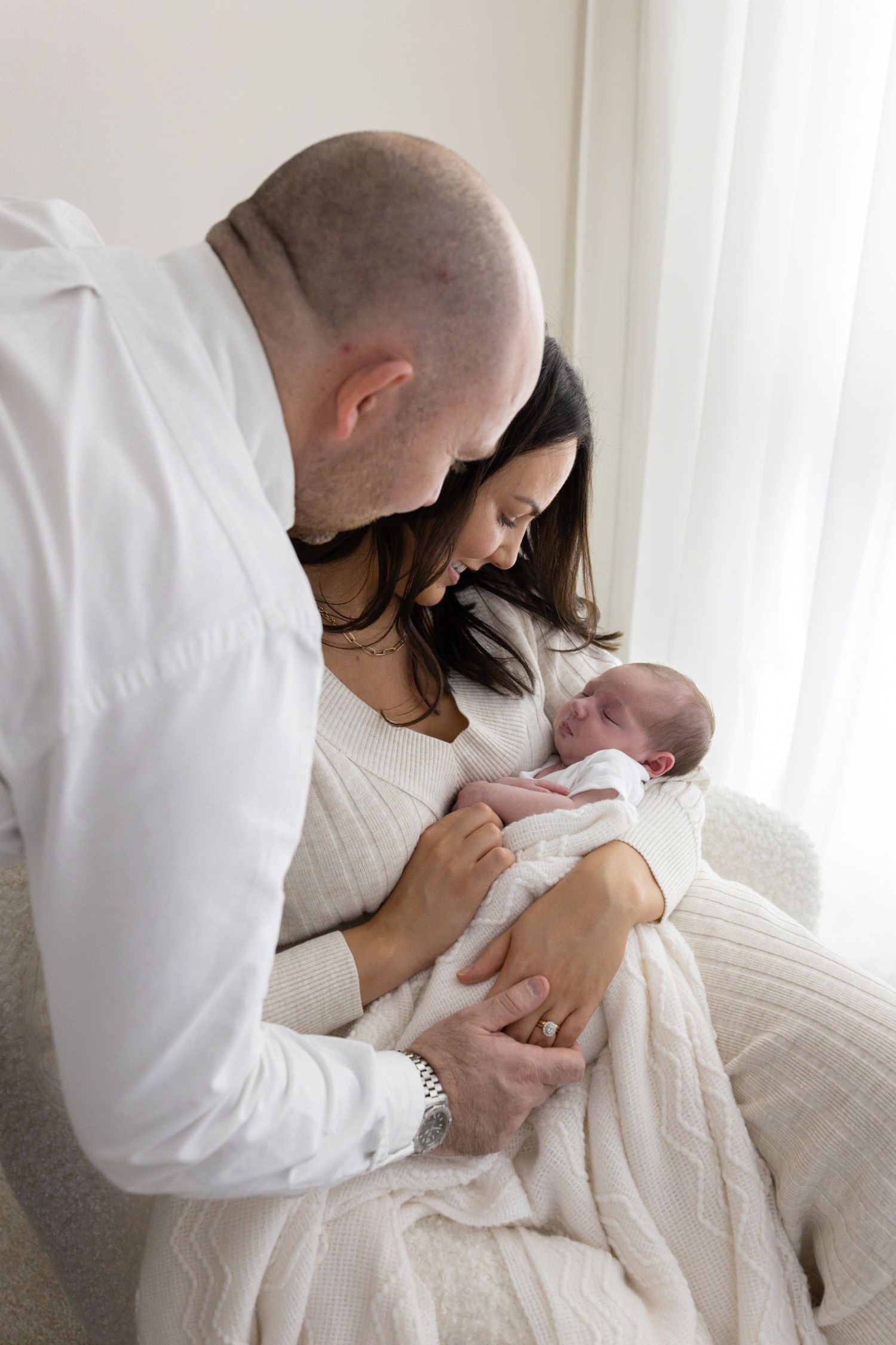 New parents leaning in together to admire their sleeping newborn baby.