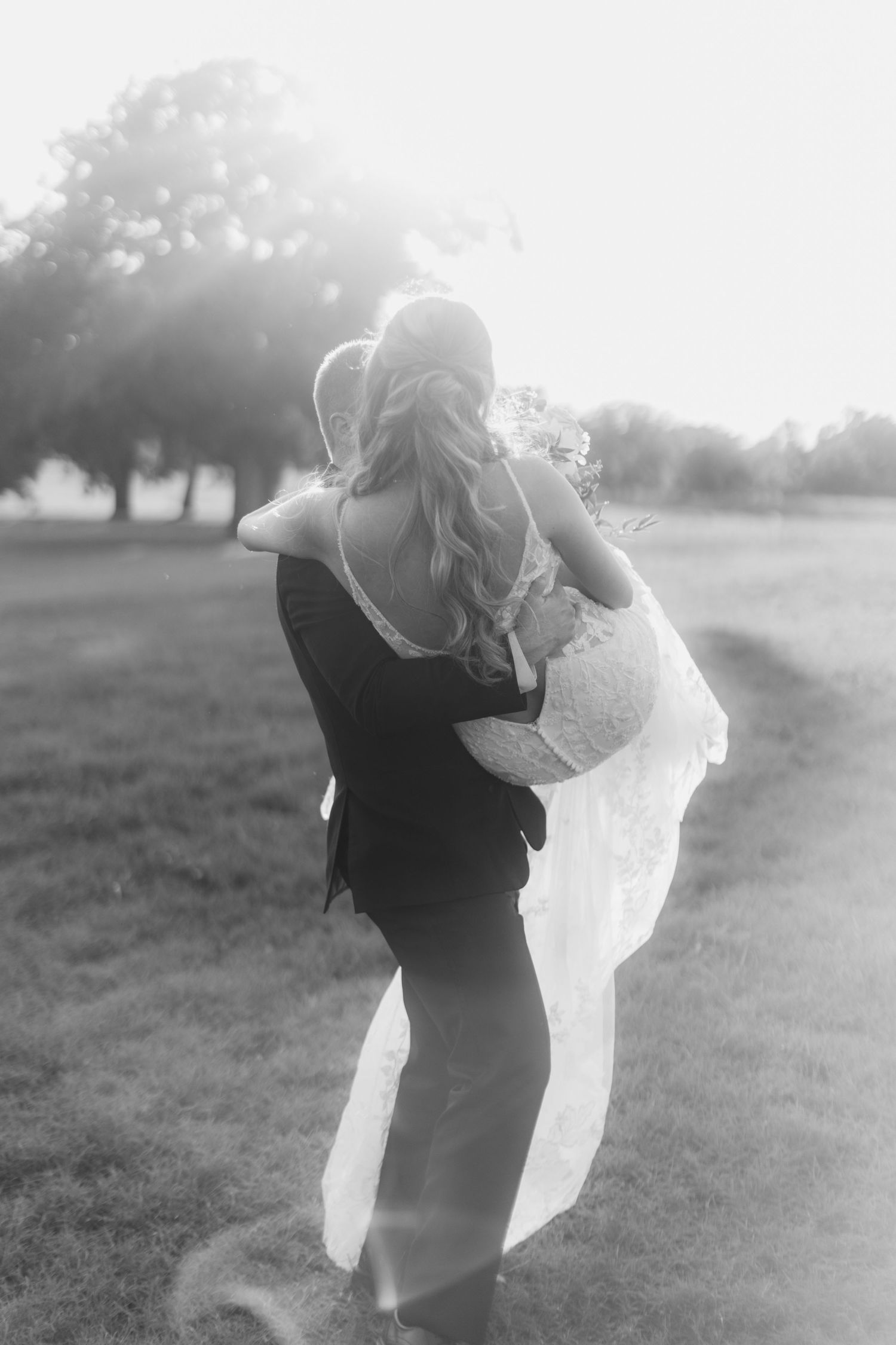 A romantic black and white photo of a couple embracing outdoors in a field with flowing dress fabric.