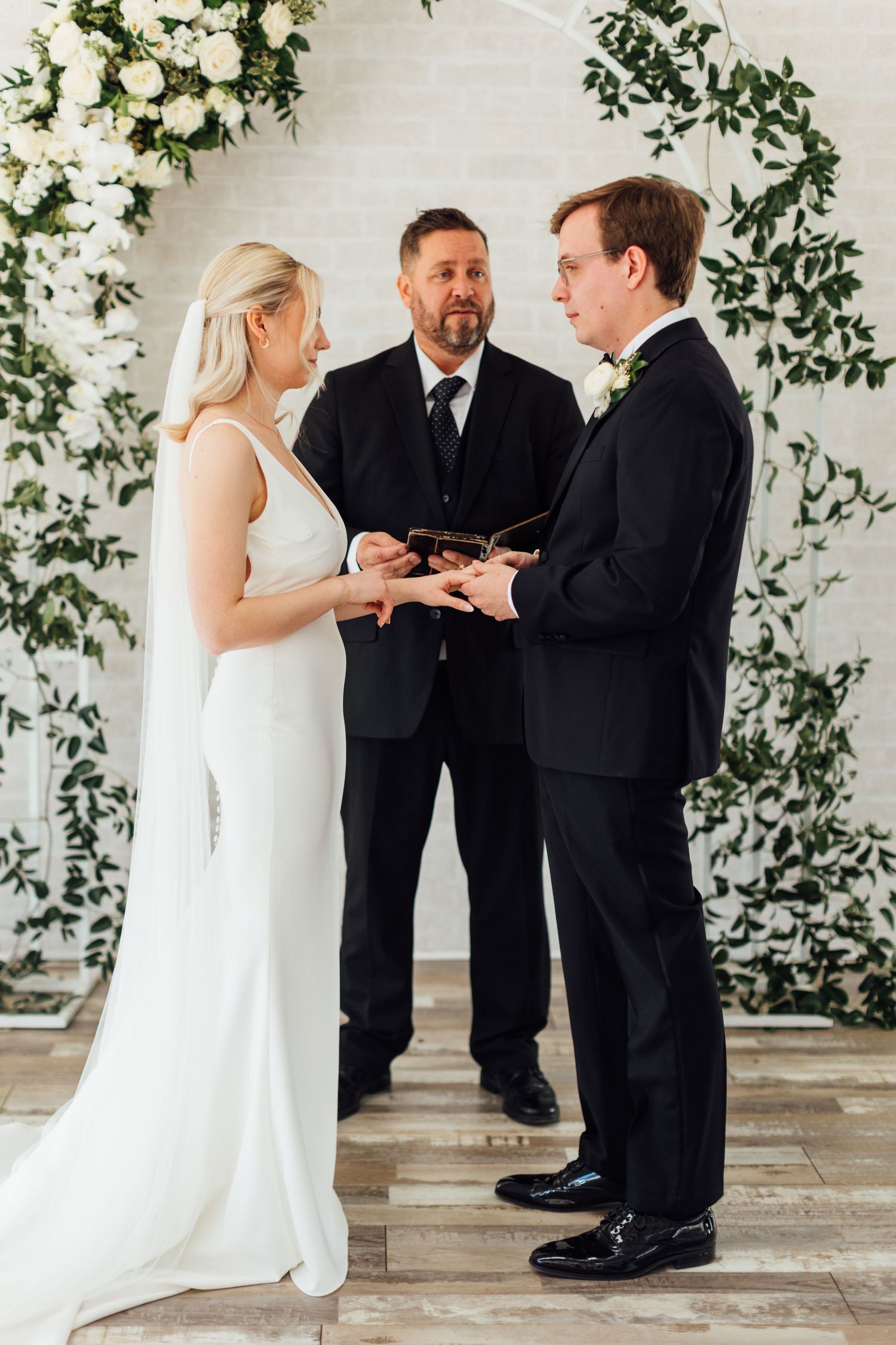 Wedding ceremony moment in white chapel decorated with lush greenery and florals.