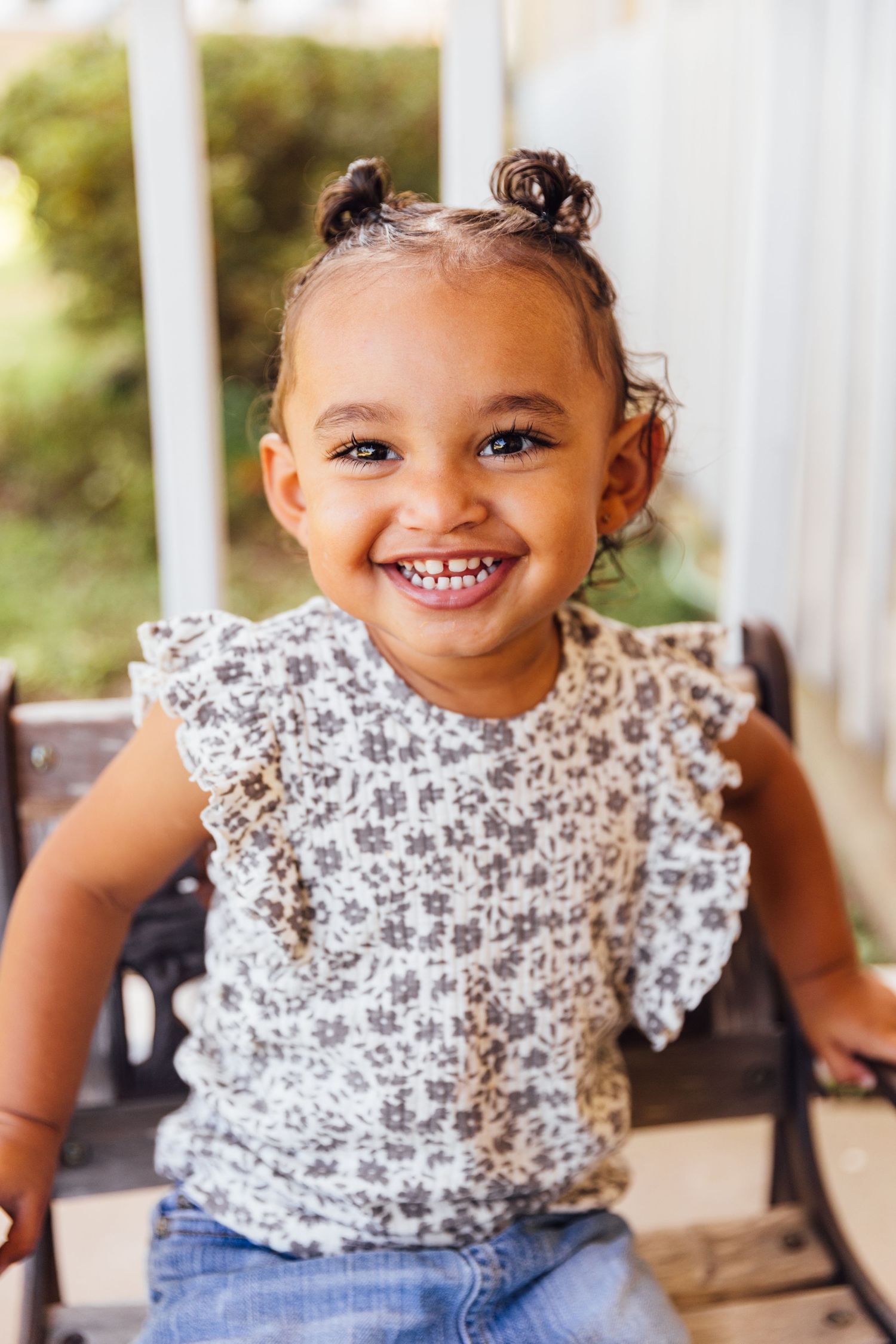 A child in a floral print top and jeans sits on a porch in a series of candid expressions.