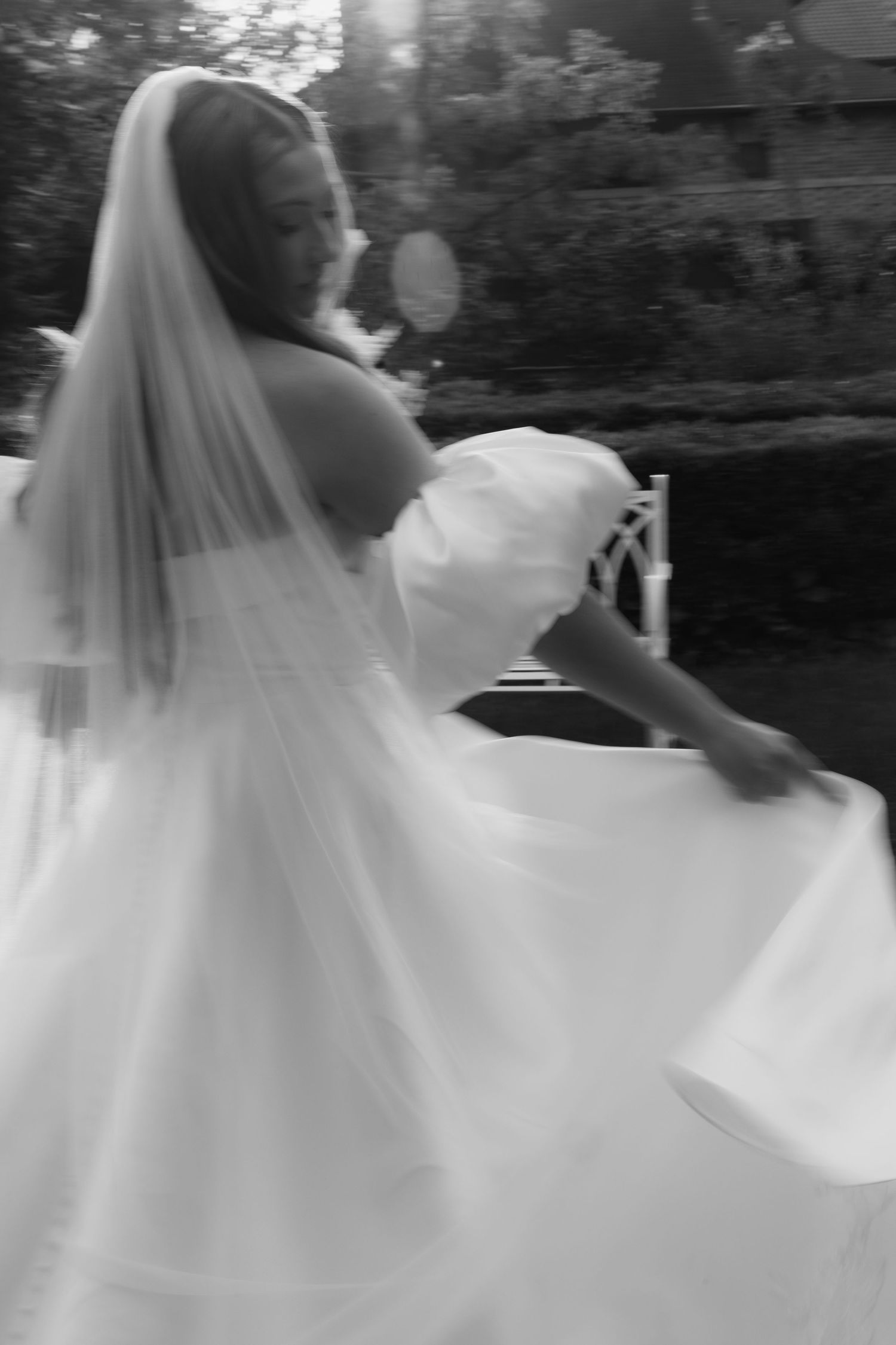 Black and white photo of a bride in a flowing wedding gown and veil, twirling outdoors.