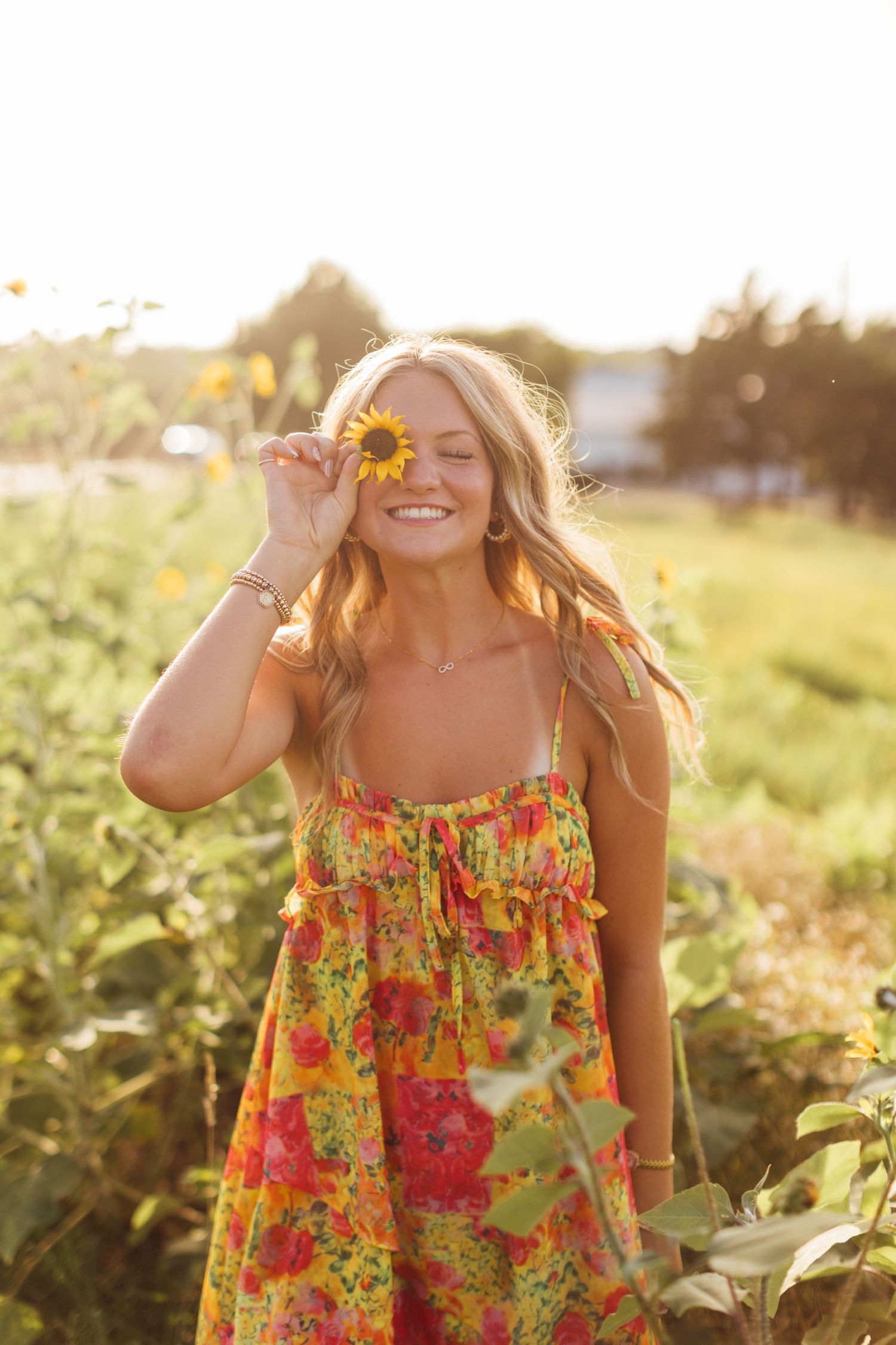 Someone in a vibrant floral sundress smiles joyfully among sunflowers at golden hour.