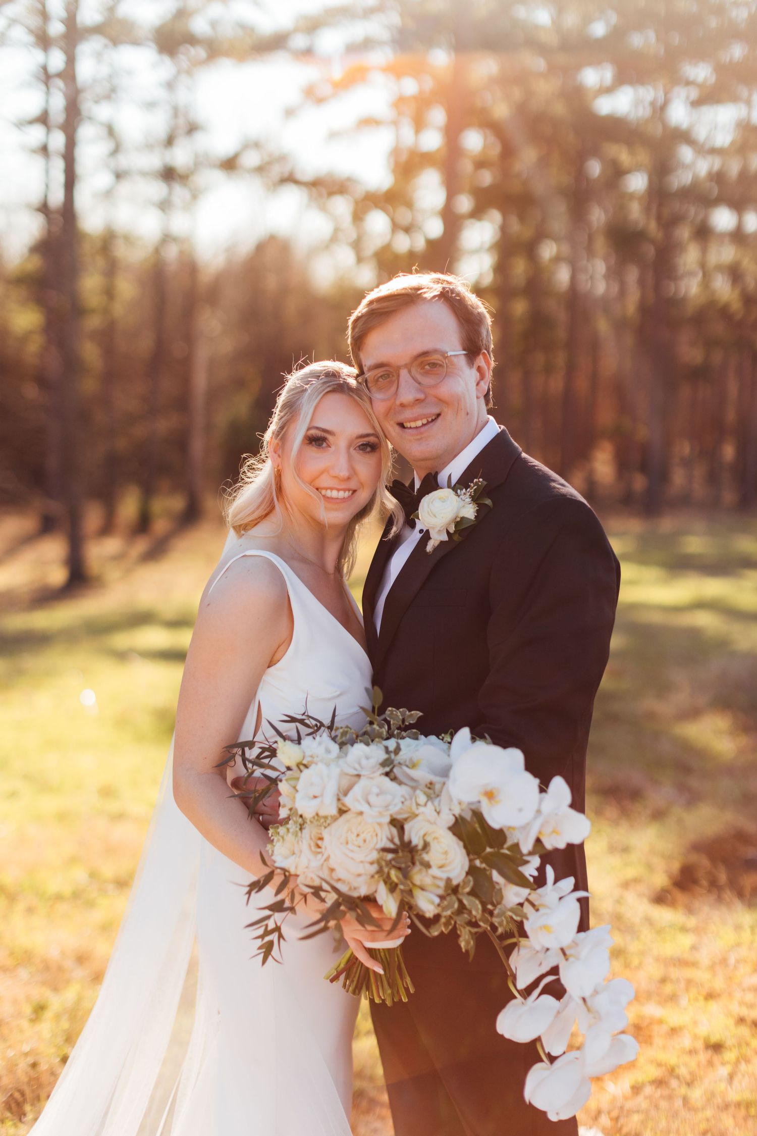 Romantic sunset portraits with bride holding white orchid bouquet against autumn backdrop.