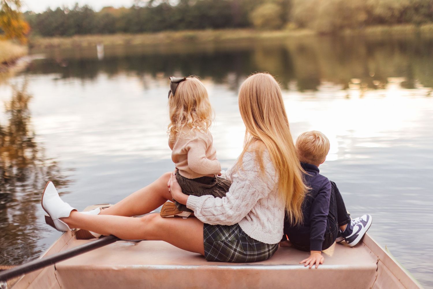 Family relaxing together on wooden dock by peaceful lake at sunset.