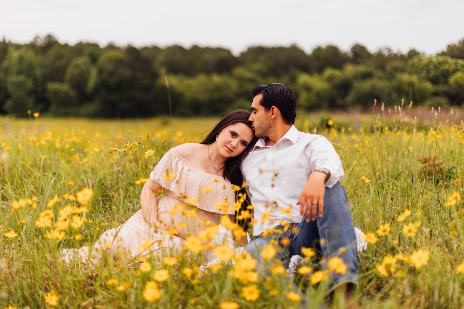 A couple sits together in a golden wildflower field during a warm summer evening.
