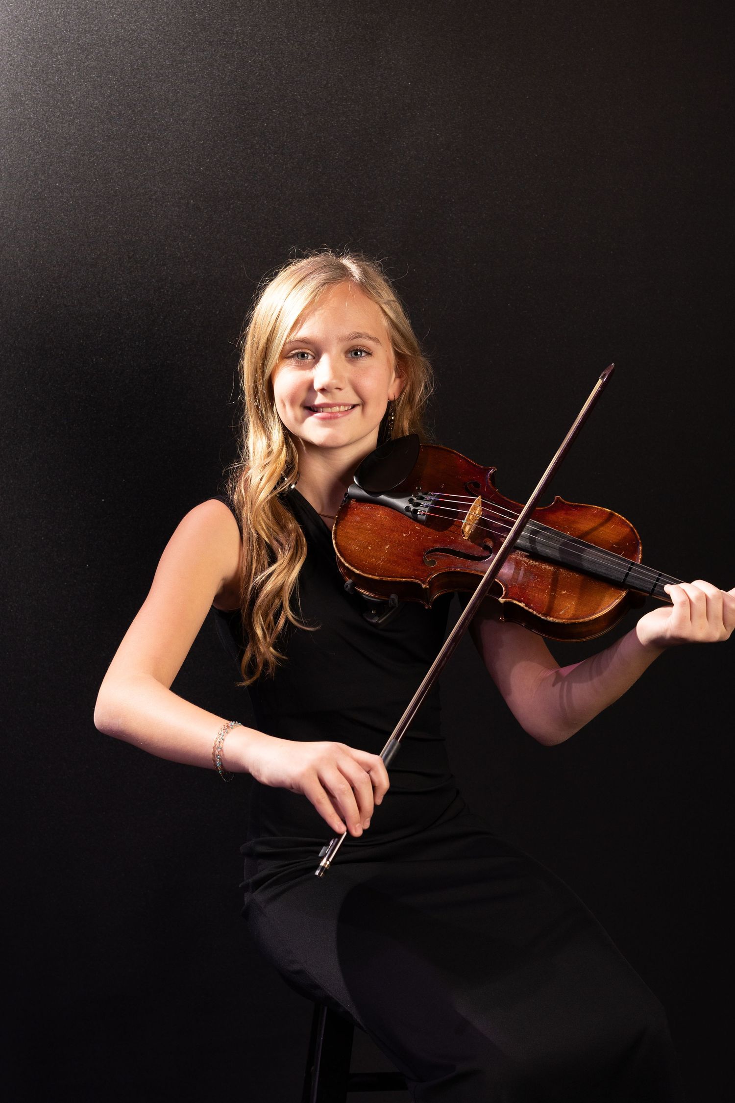 A musician in a black dress performs on violin against a dark background.