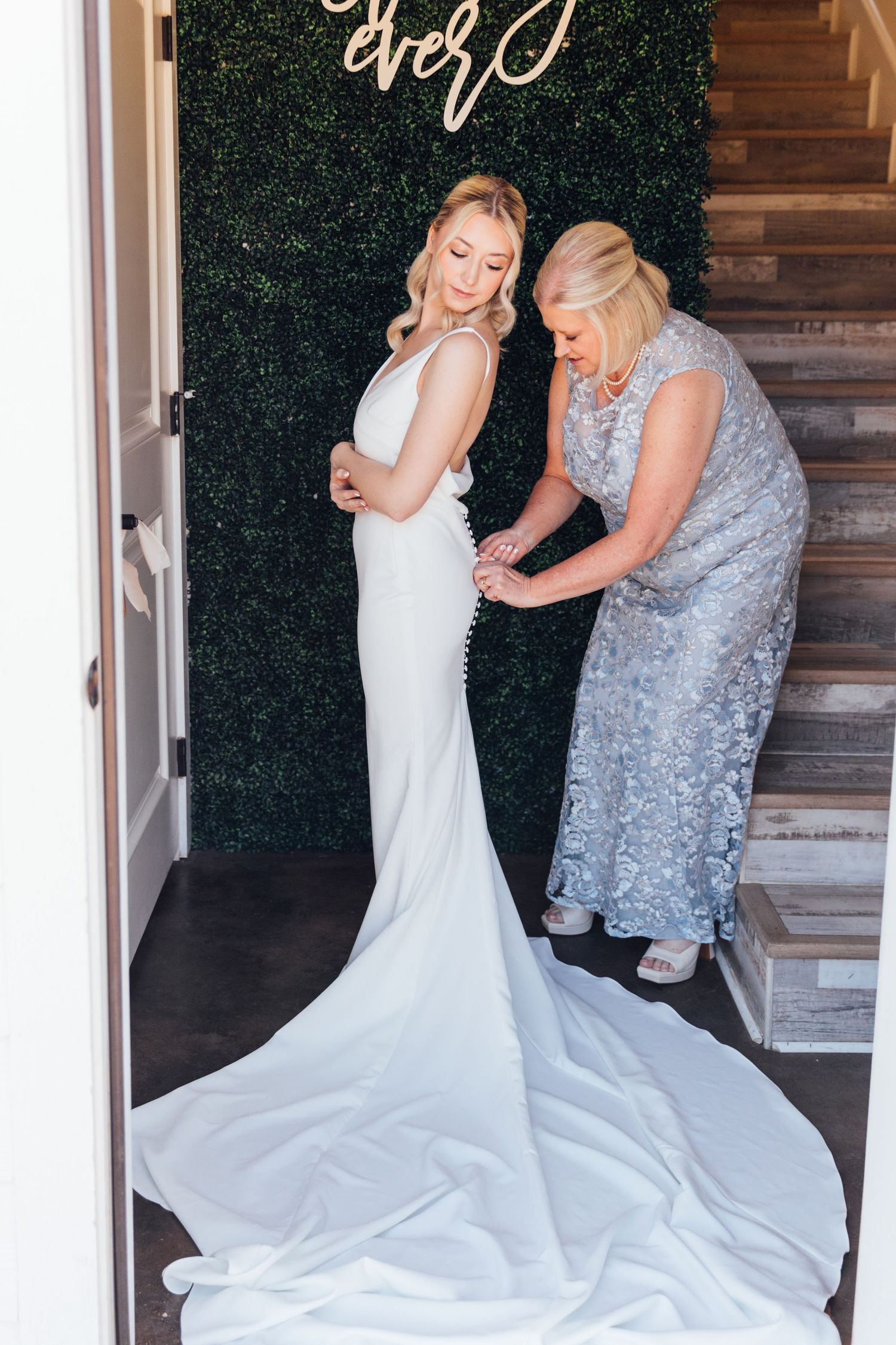 Final wedding dress fitting against green hedge backdrop.