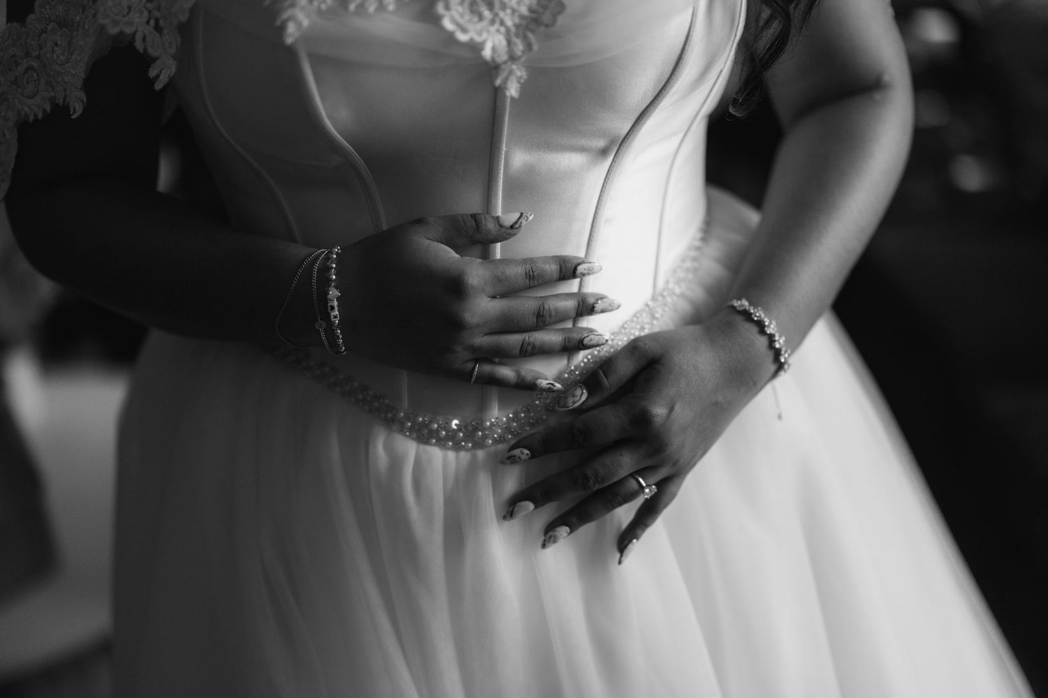 Black and white photo of a bride holding a bouquet, wearing bracelets and rings, in a white wedding gown.