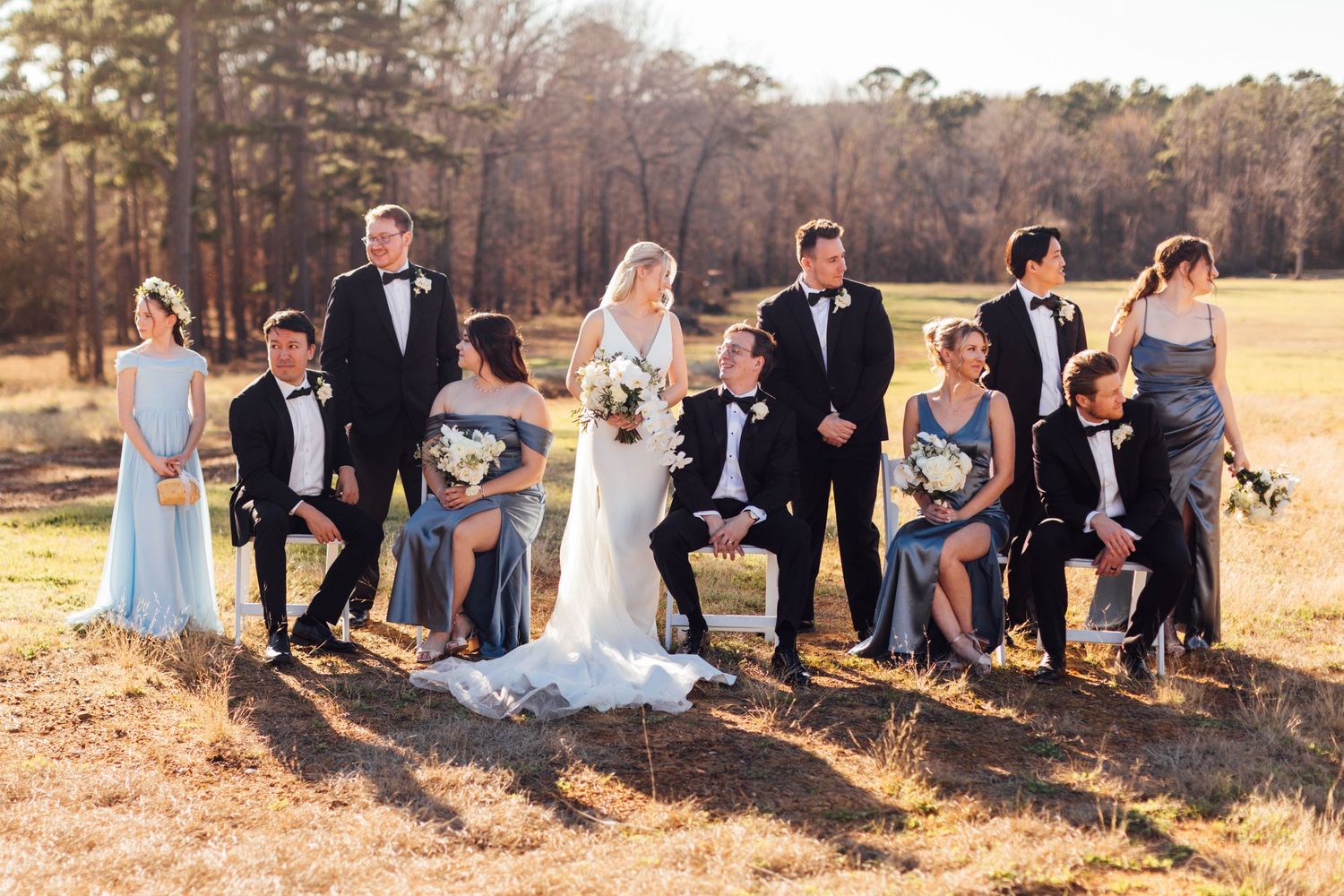 Wedding party lounges together on hillside with golden sunlight and trees in background.