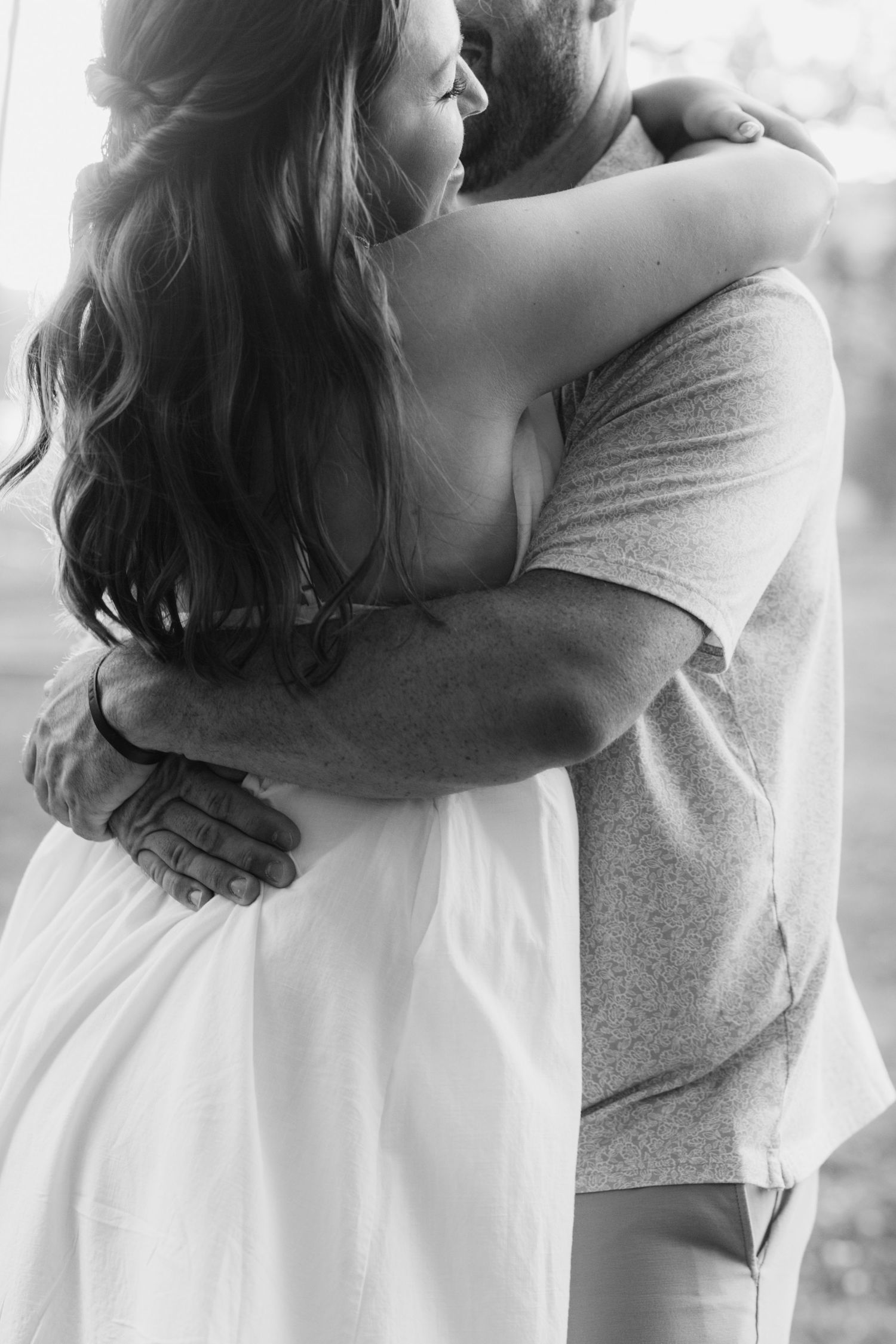 Black and white photo of a couple sharing a tender embrace, woman in white dress with long hair.