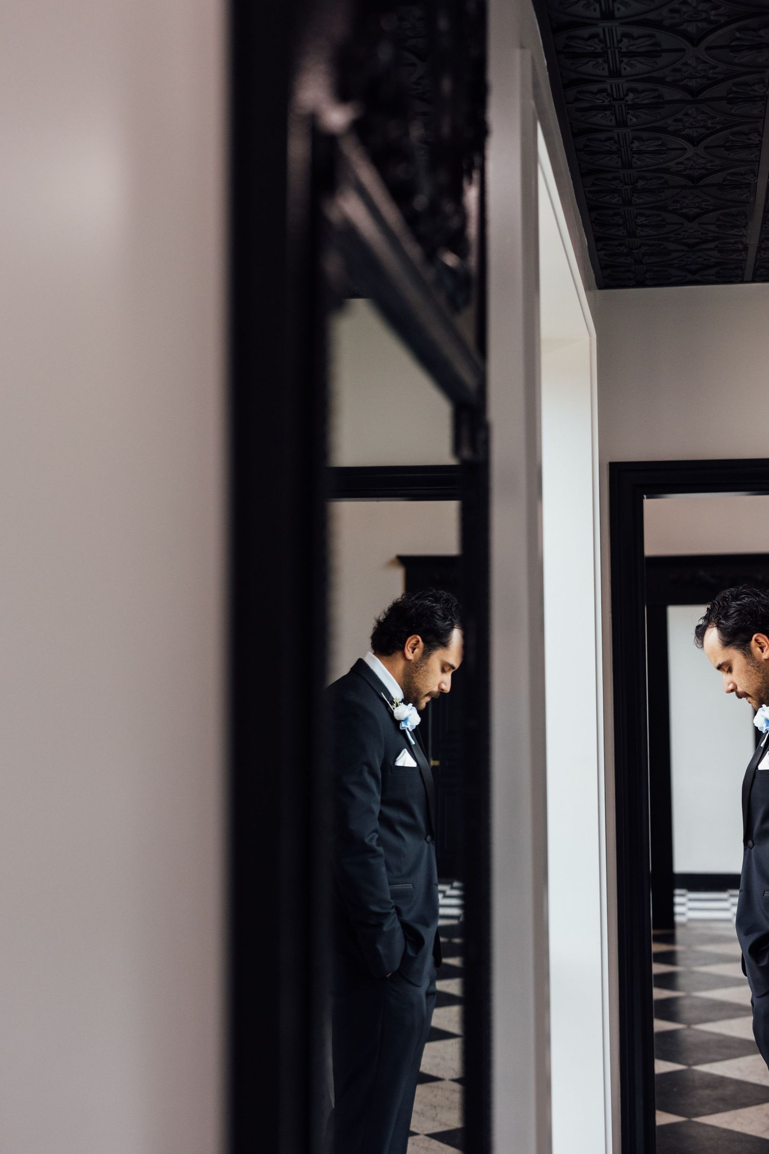 Two men in dark suits standing in an elegant hallway with checkered floors and decorative black ceiling.