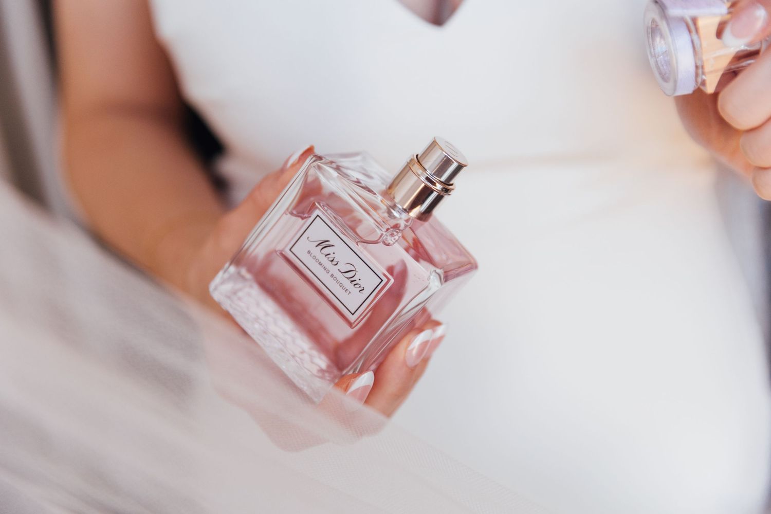 Elegant perfume bottle held by bride in white dress.