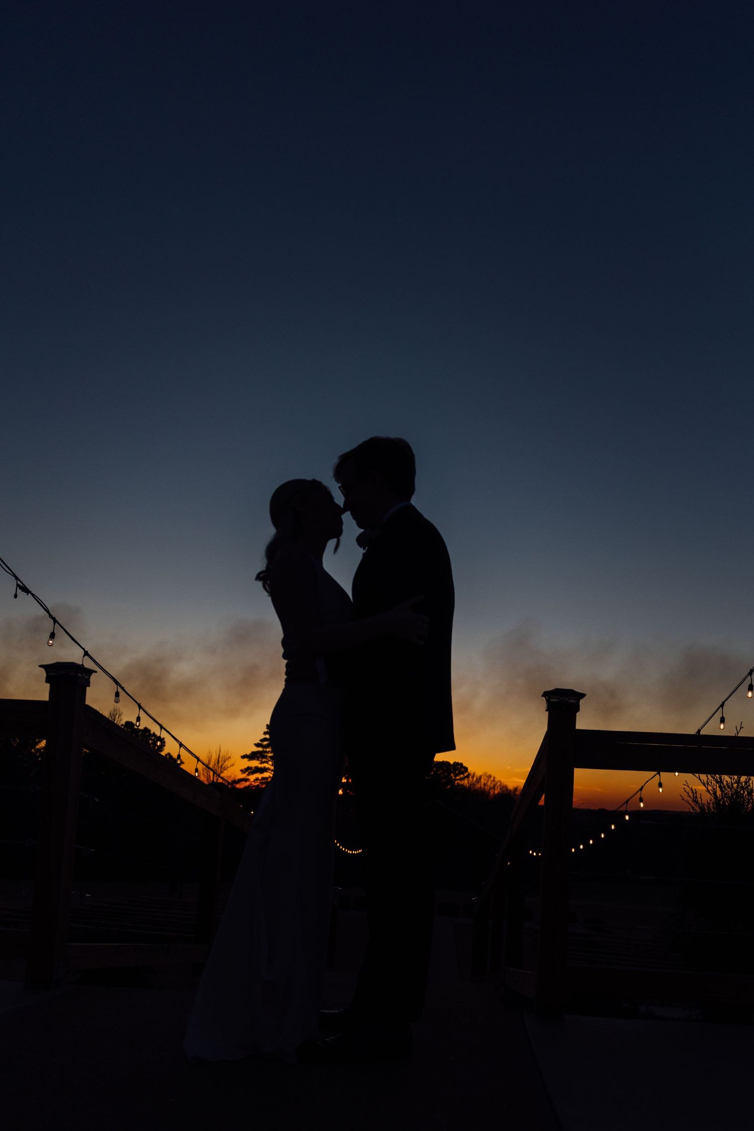Silhouettes of wedding couple against dramatic sunset sky.