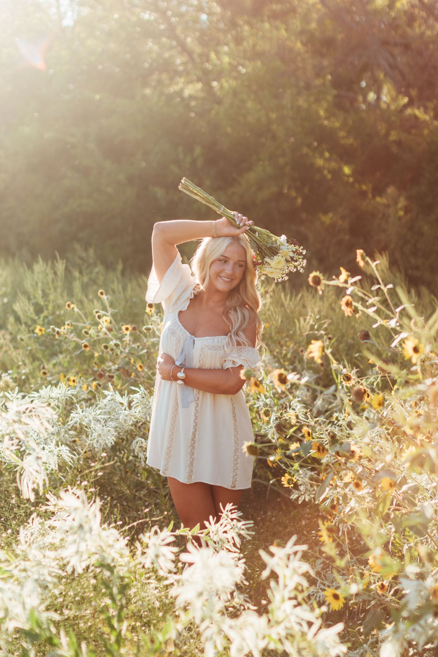 A person in a white dress poses in a sunlit wildflower meadow during golden hour.
