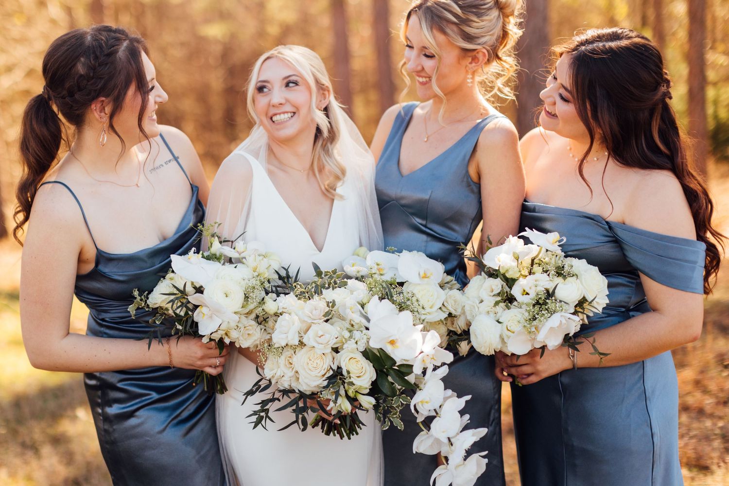 Bridesmaids in blue dresses hold white floral bouquets while sharing joyful moments.