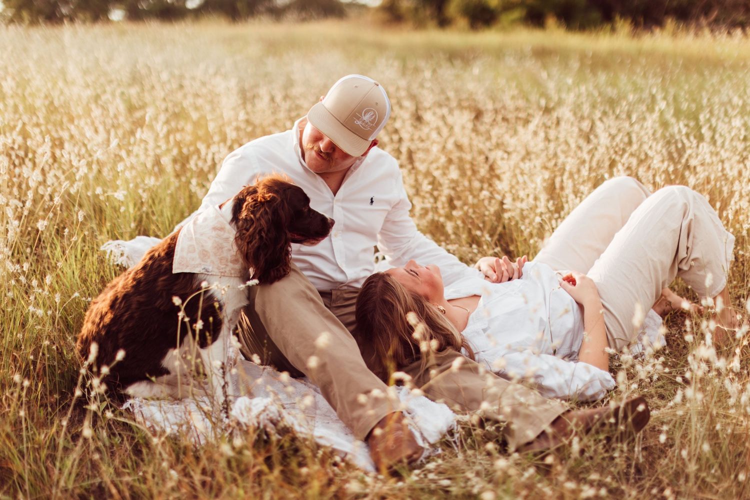 A pair enjoys a romantic picnic date in a sunlit meadow surrounded by tall golden grass and wildflowers.