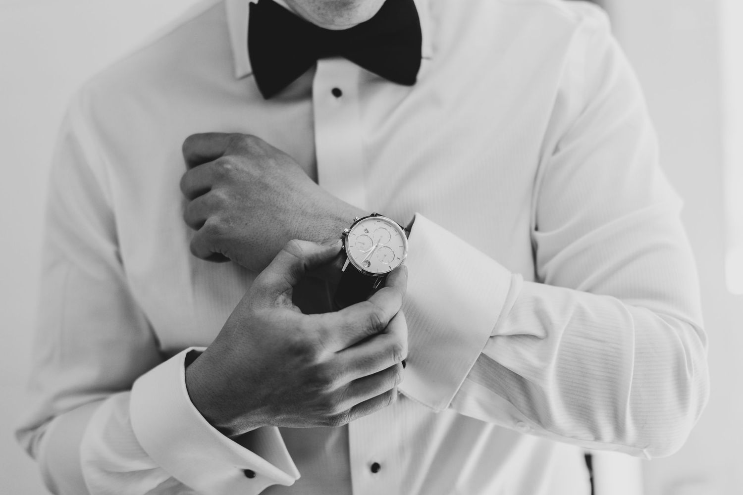 Groom adjusting cufflink on white dress shirt with bow tie.