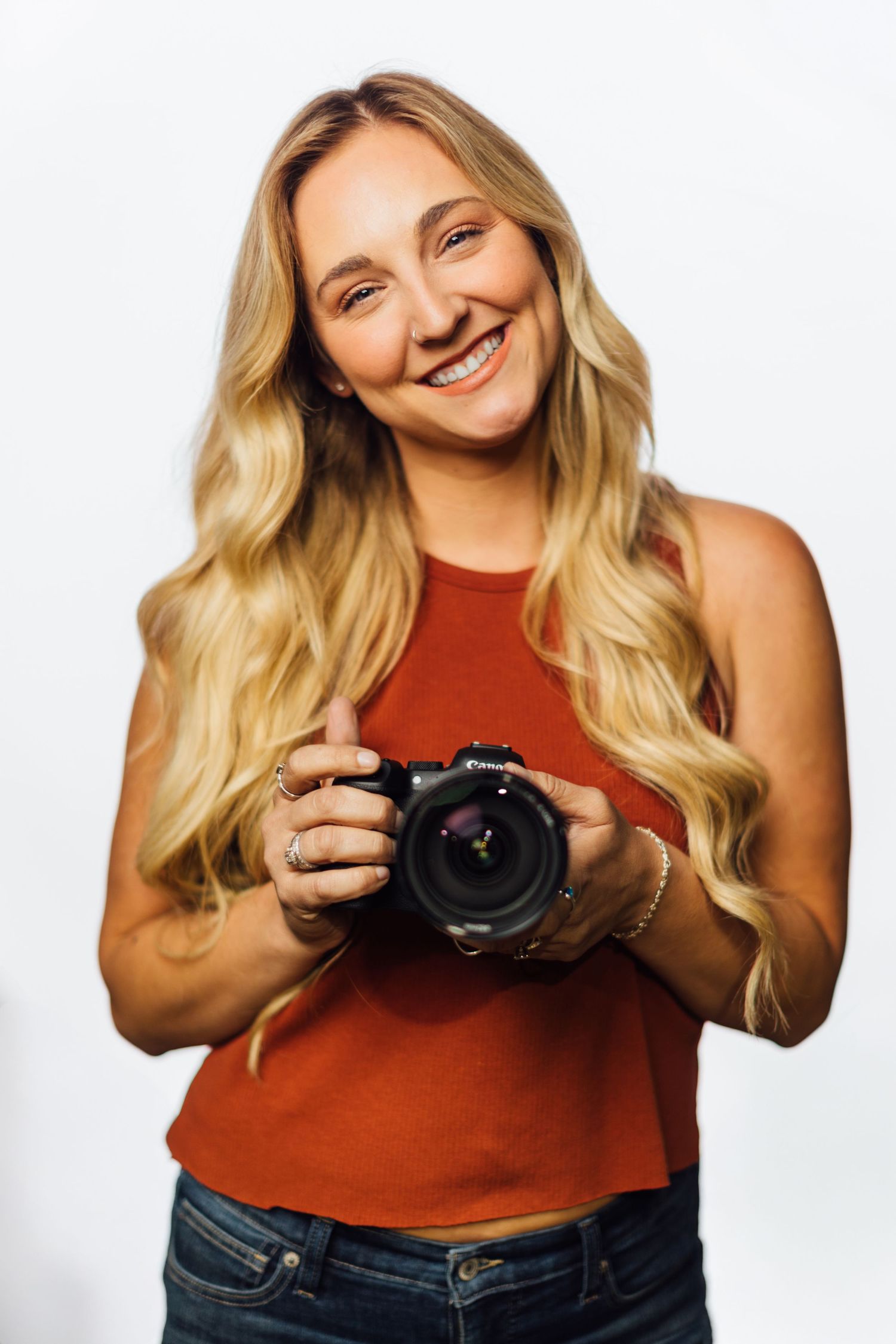 Photographer in a rust-colored tank top holds a DSLR camera while posing against a white backdrop in multiple shots.
