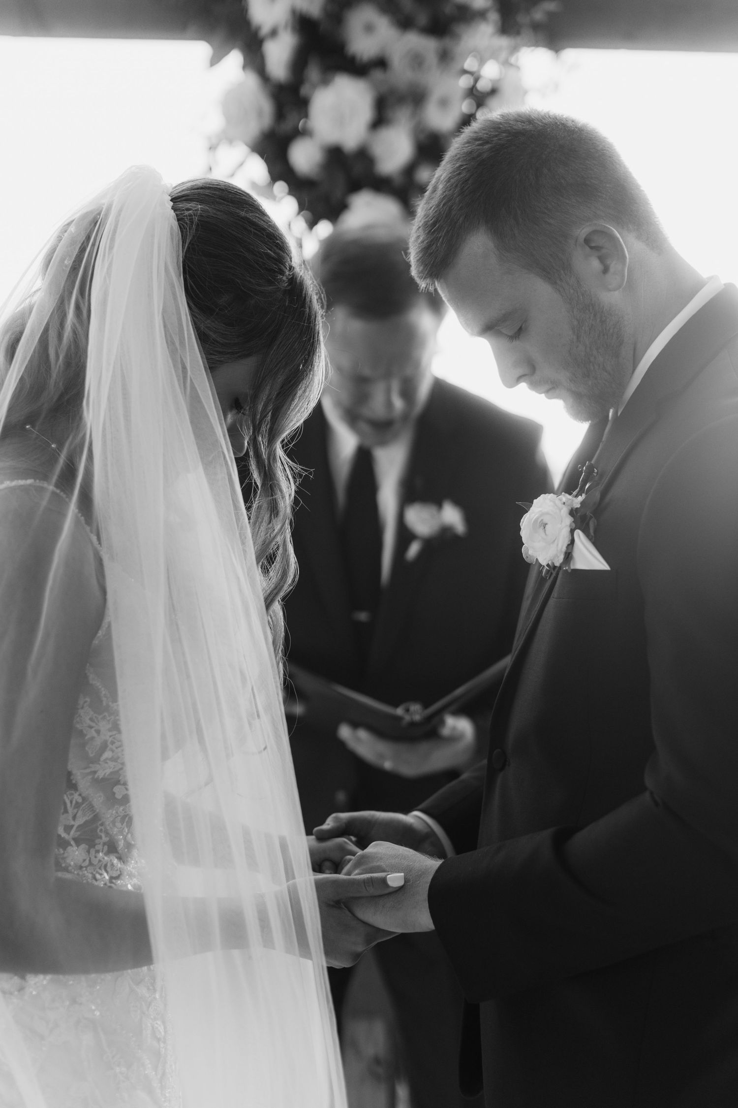 A touching black and white wedding ceremony moment as couple exchanges vows with officiant in background.