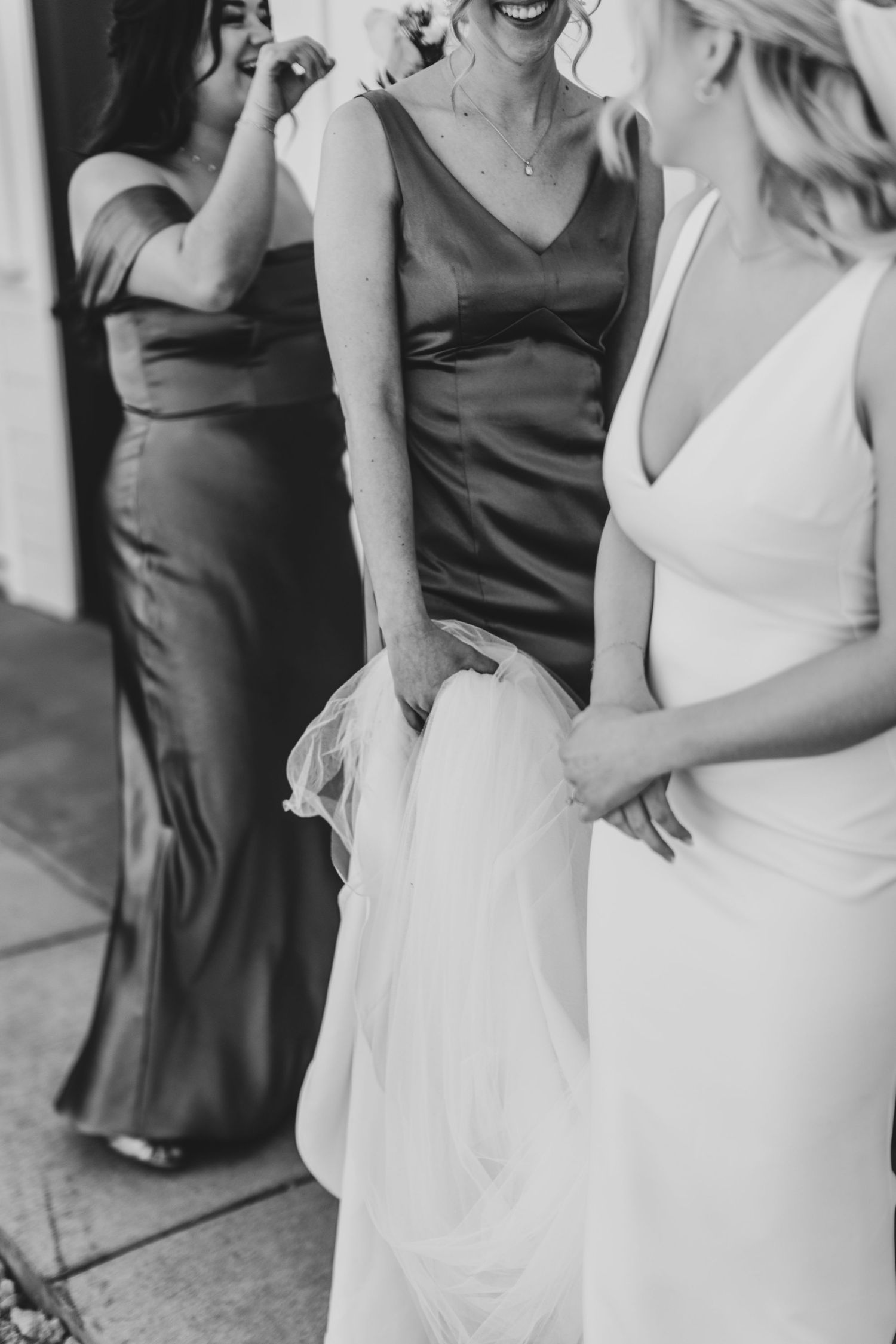 Bridal party wearing contrasting white and dark dresses laughs together in elegant celebration.