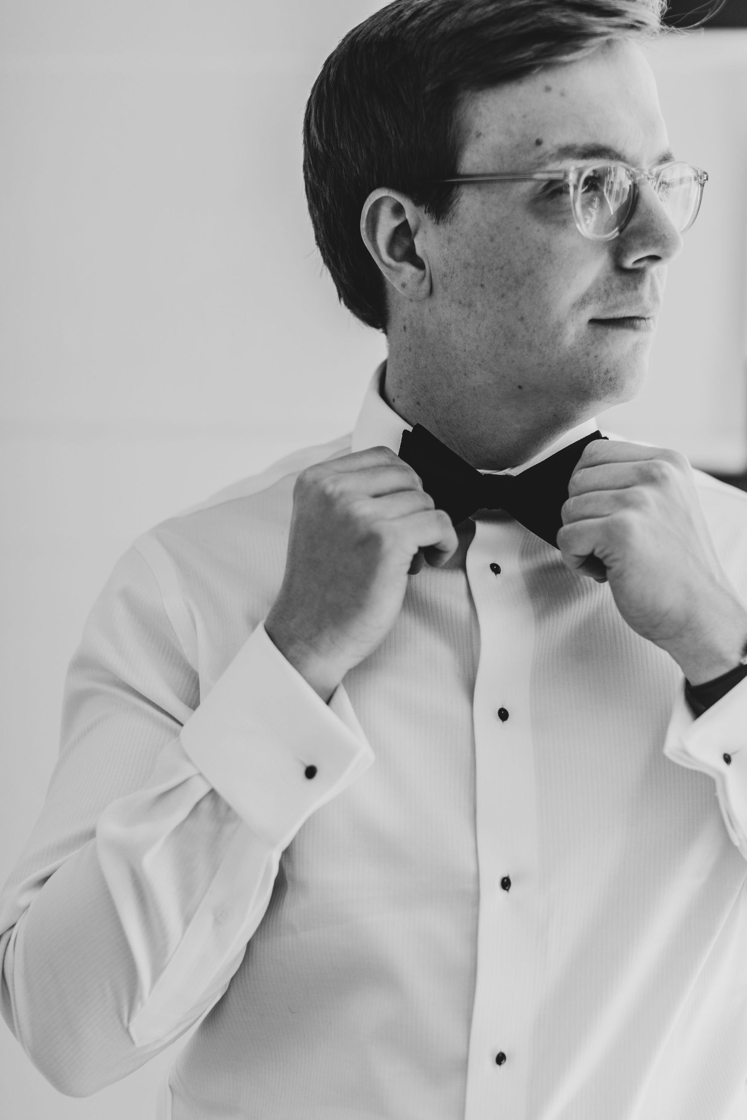 Groom in white shirt and bow tie adjusting collar.